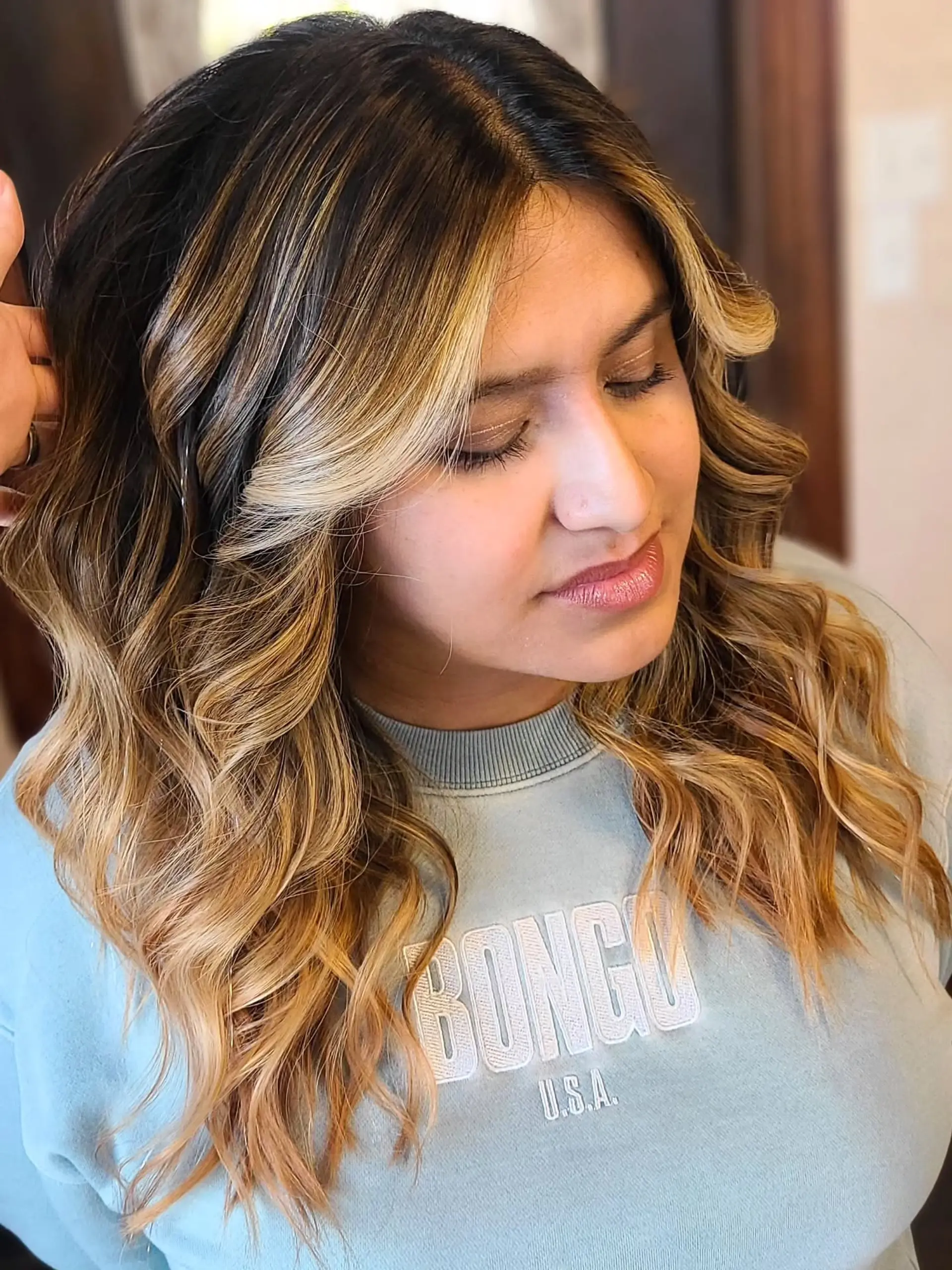Long, wavy hair with a blended balayage coloring technique that transitions from dark roots to warm caramel and golden blonde ends, styled with soft, loose waves. 3