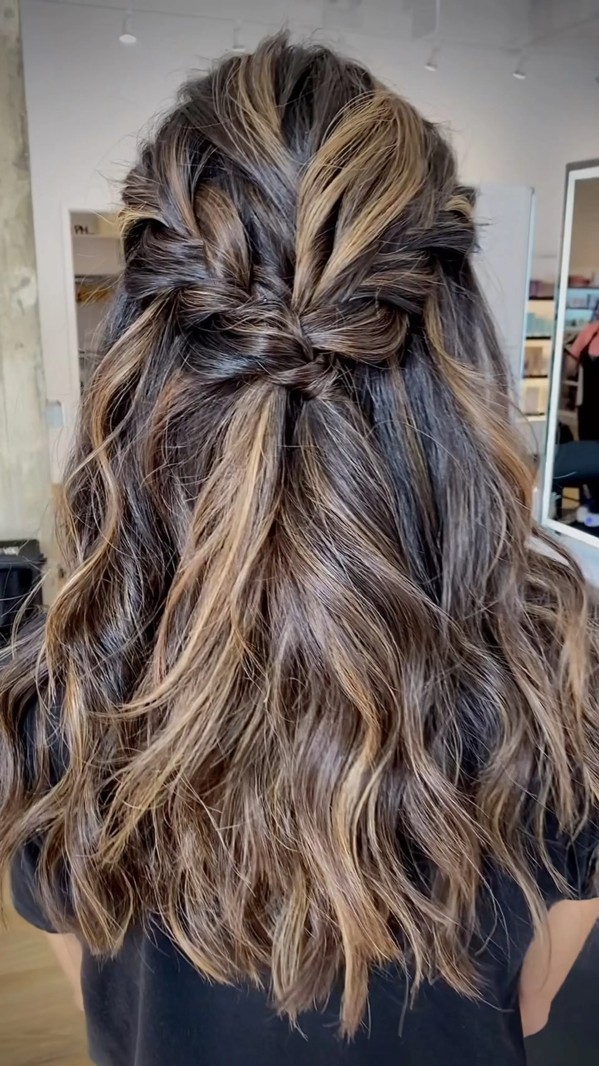 Long dark brown hair styled in a half-up twisted knot with dimensional caramel and blonde balayage highlights over soft waves. 1
