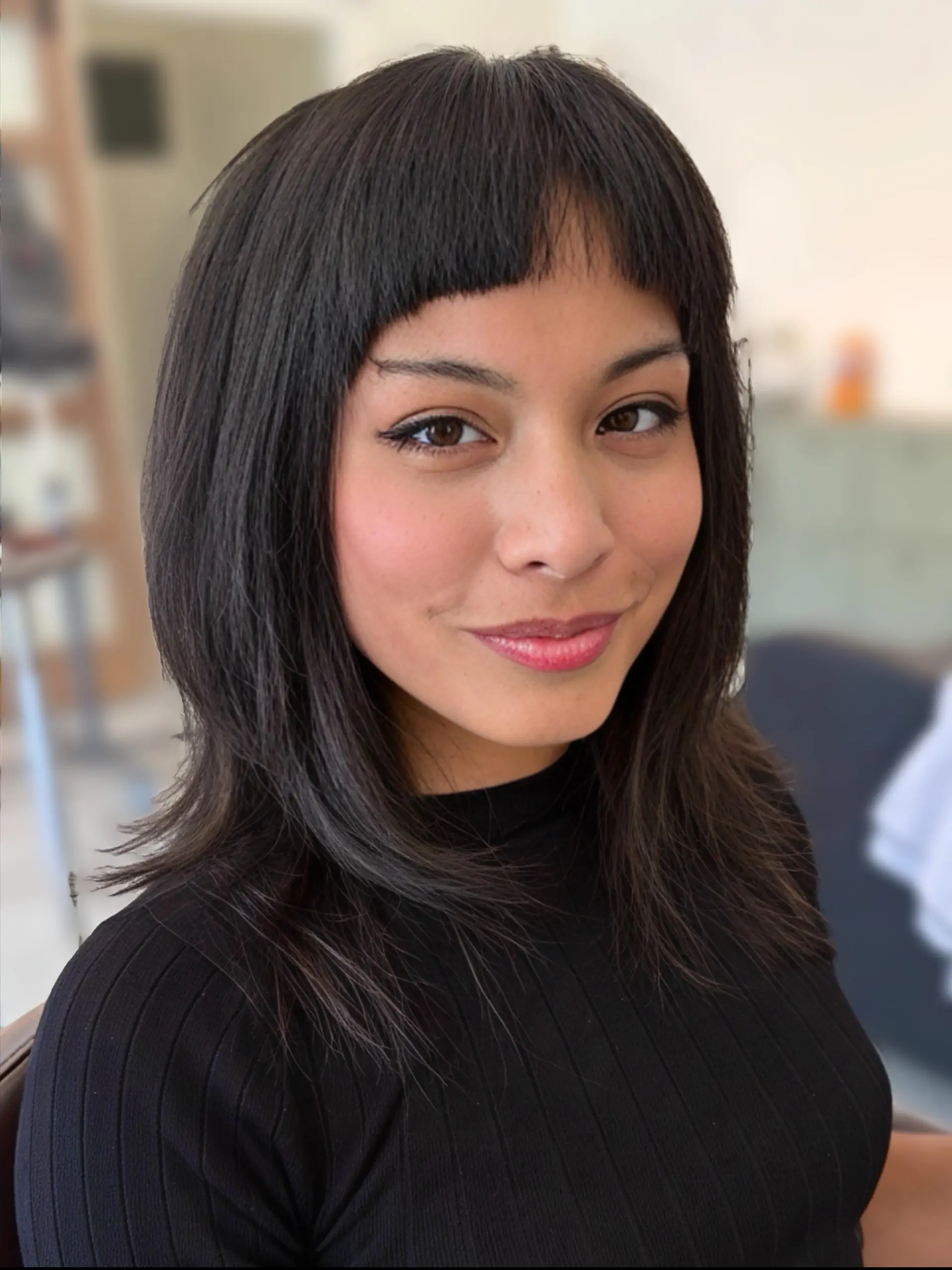 A medium-length layered haircut styled straight with distinctive baby micro bangs. 1