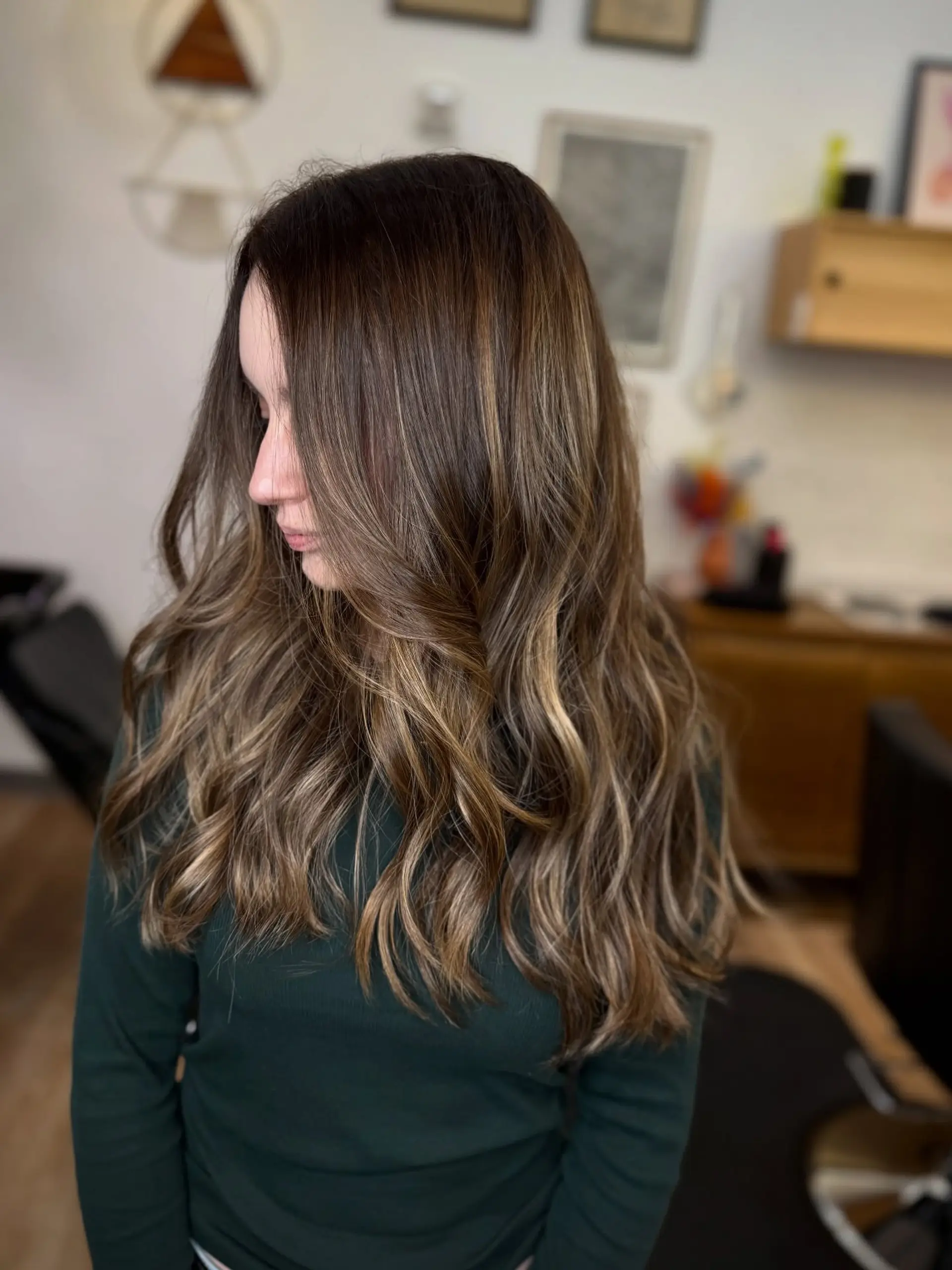 Long dark brown hair highlighted with soft caramel balayage and styled into loose waves. 1