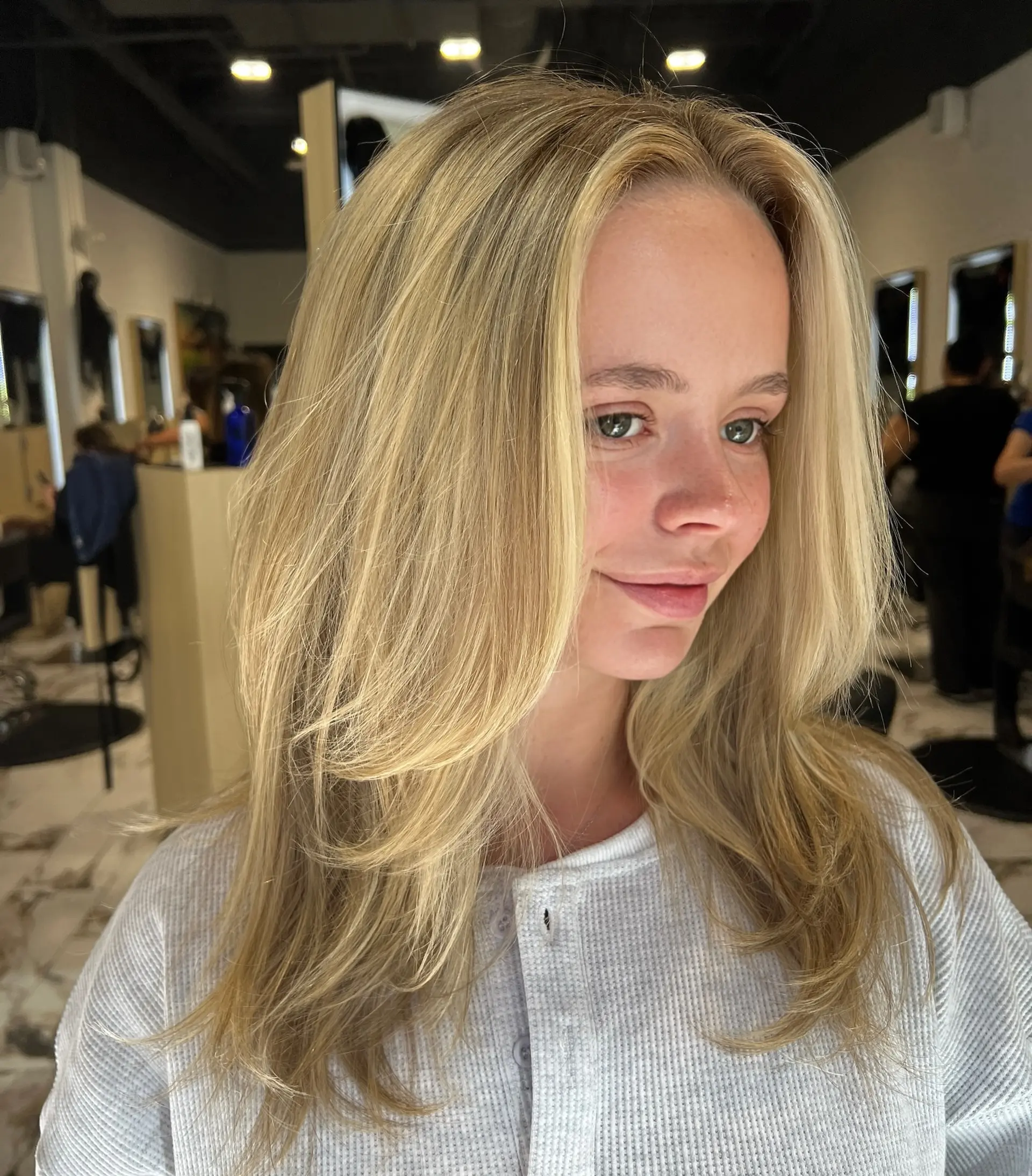 Long dimensional blonde hair featuring face-framing layers and a bouncy, smooth blowout with turned-out ends. 1
