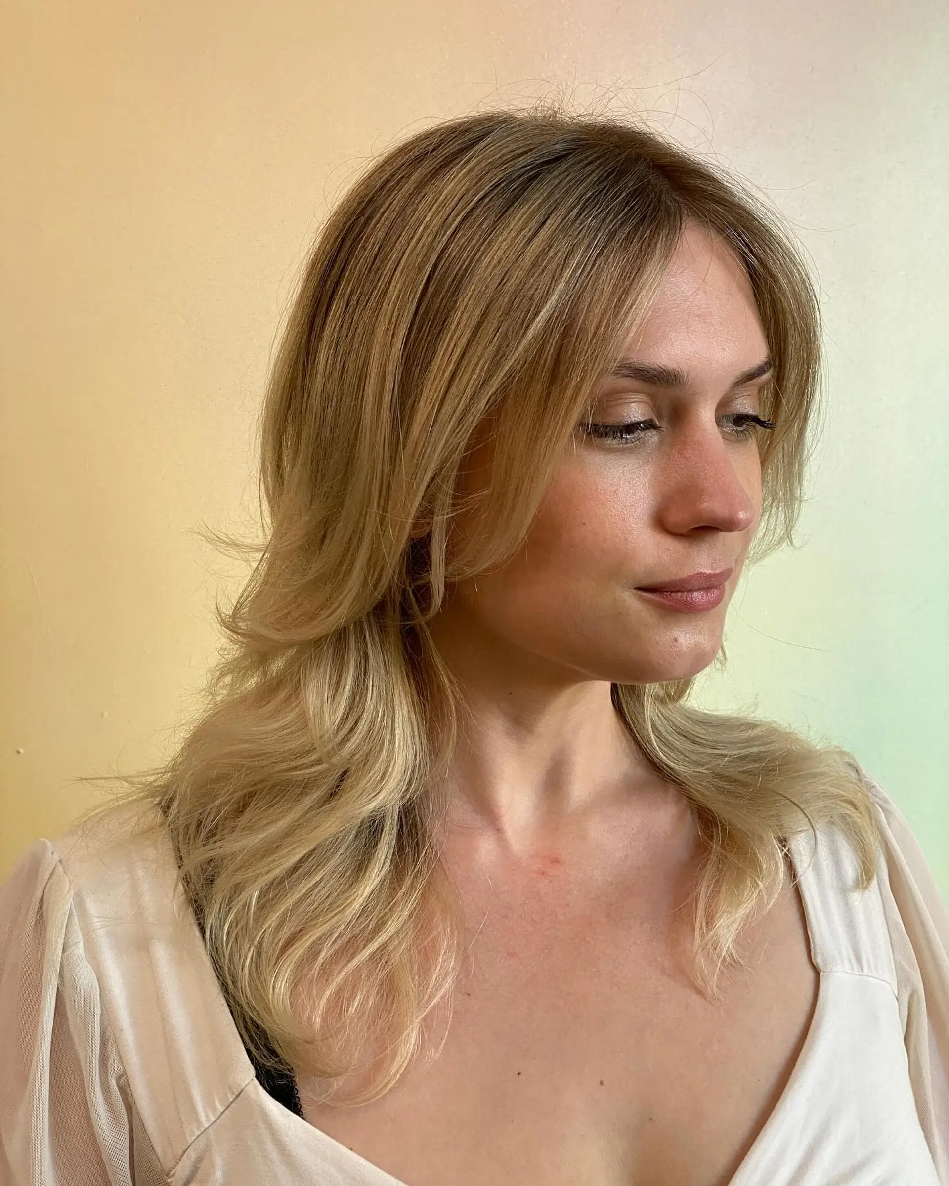 Medium-length warm blonde hair with blended highlights, a soft root tap, and center-parted curtain bangs. 1