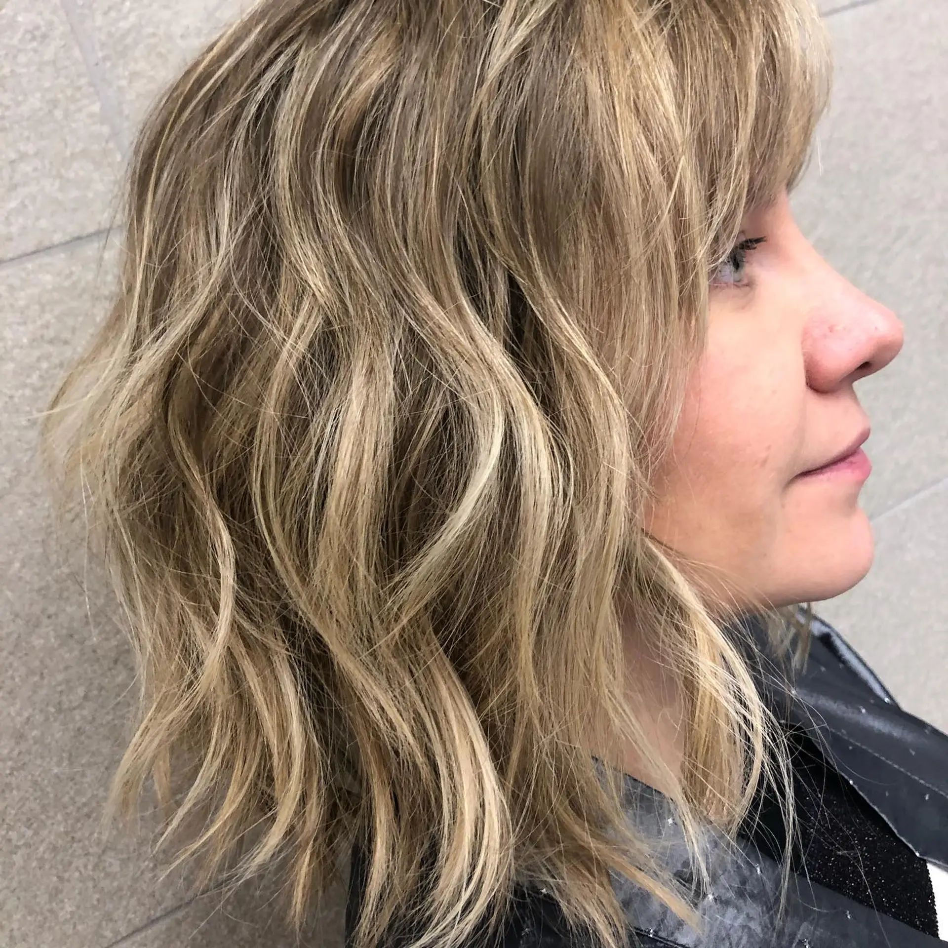 A textured shoulder-length wavy lob featuring dimensional blonde highlights and soft, piecey bangs. 1