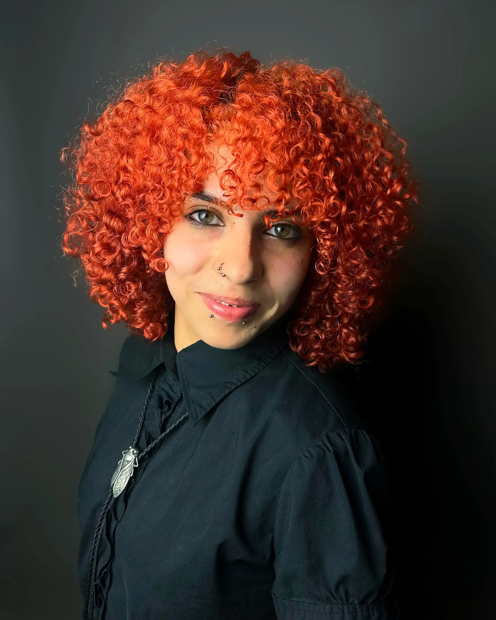 A rounded, voluminous curly bob cut featuring tight ringlets, full curly bangs, and a vibrant fiery copper-orange color. 1