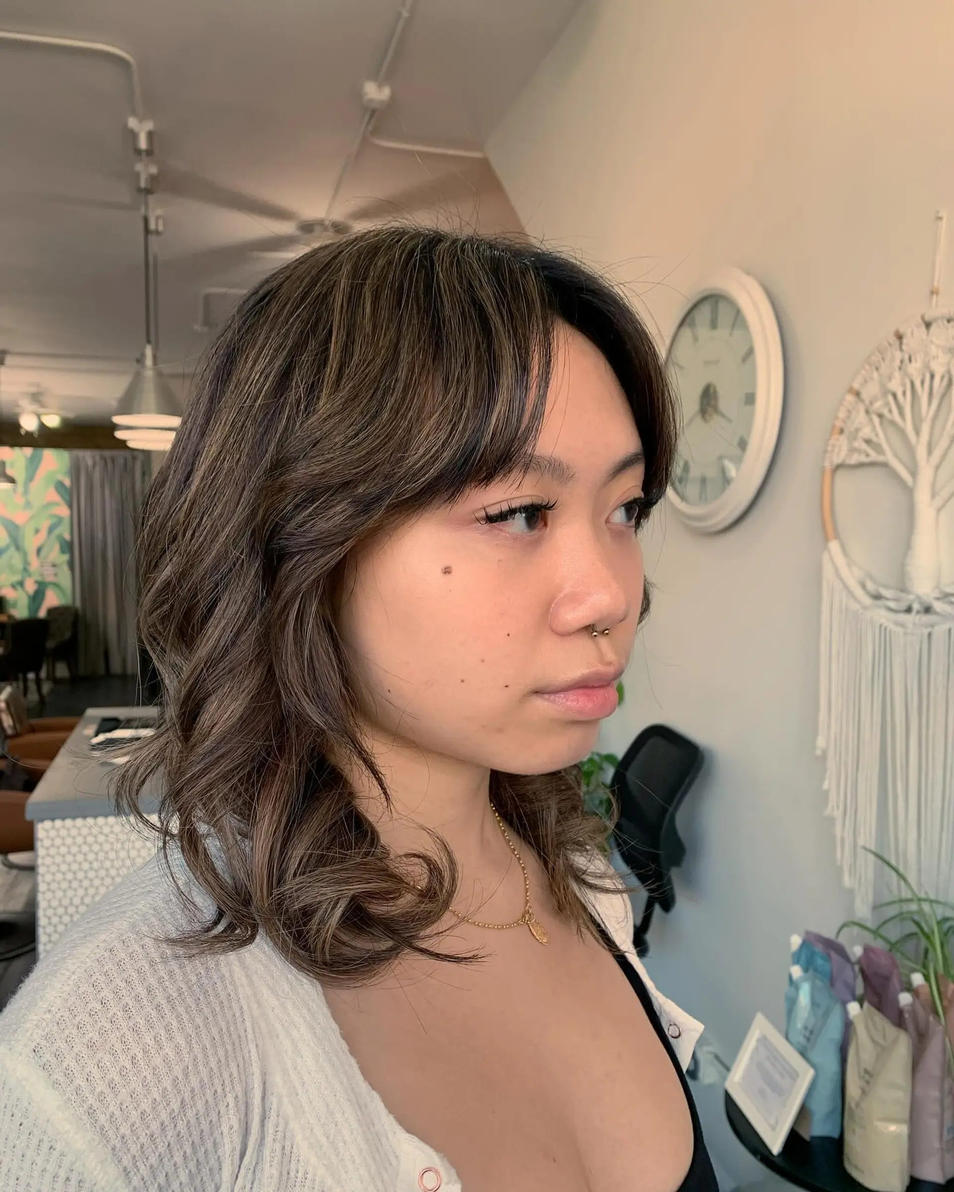 Medium-length layered haircut featuring soft, face-framing curtain bangs, subtle flipped ends, and a dimensional cool-toned milk tea bronde color. 1
