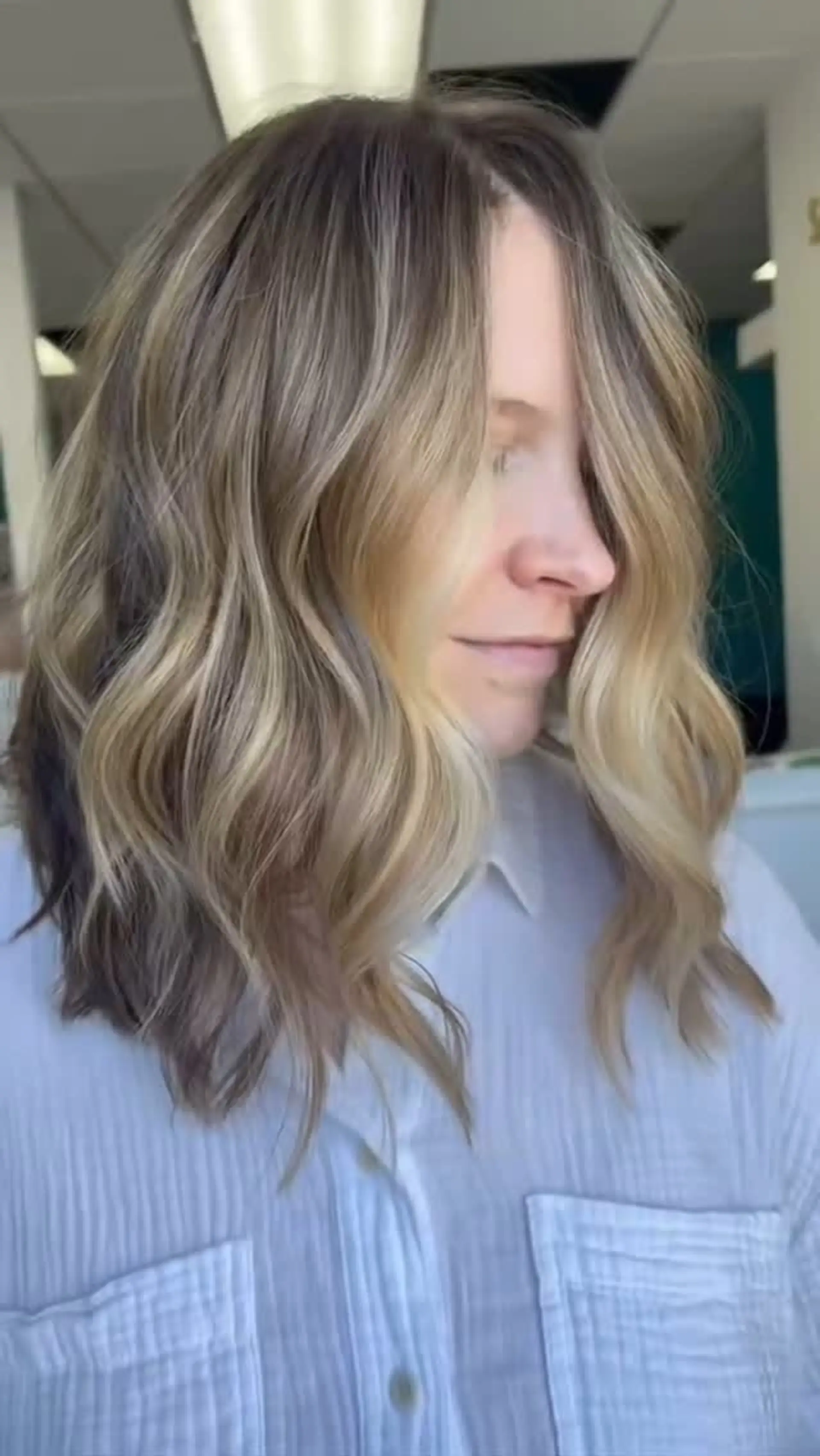 A textured, shoulder-length lob styled in loose beach waves with a soft center part and face-framing blonde highlights. 1