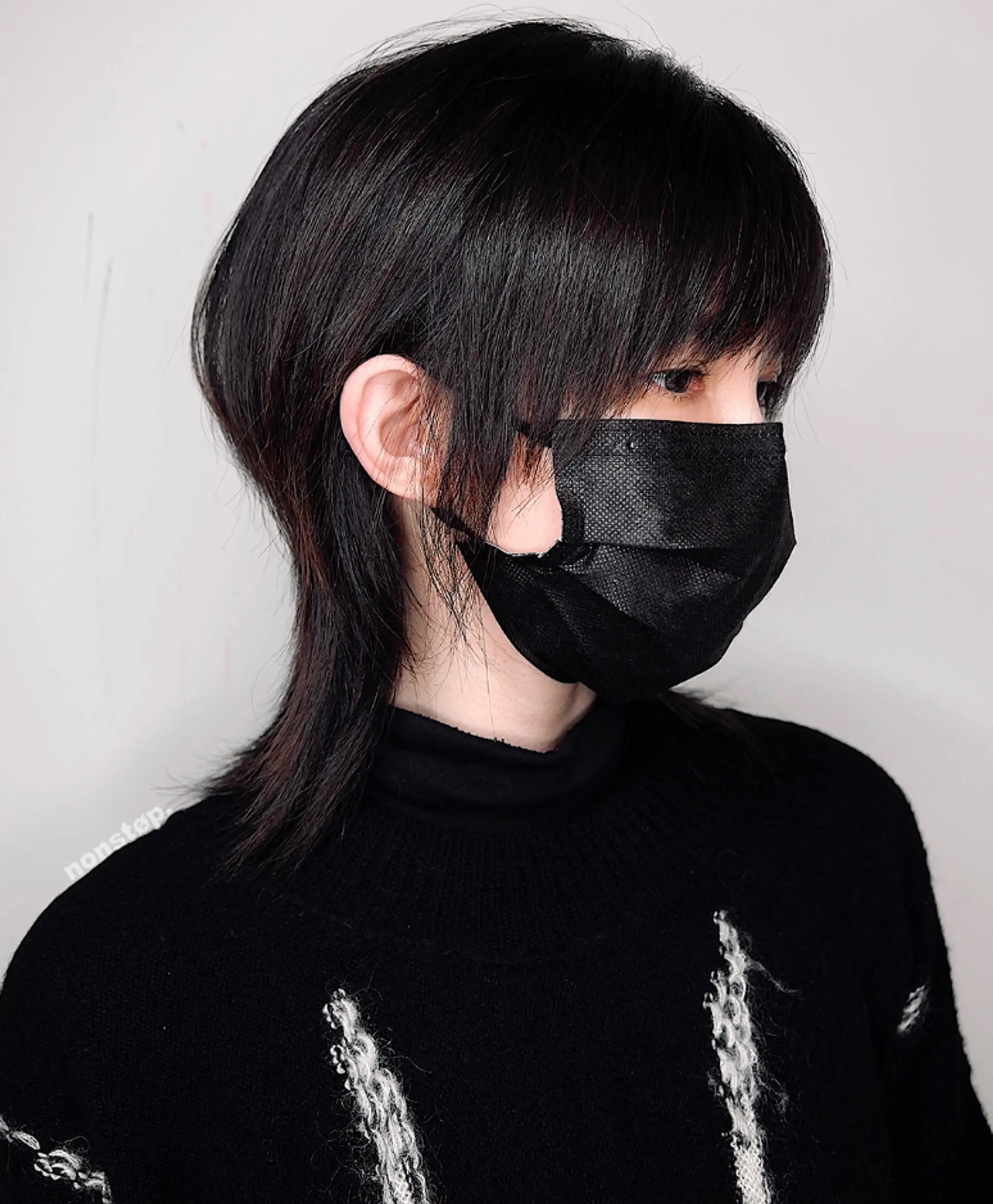 The hairstyle features a modern shag with sleek, straight, black hair. It has an edgy, layered cut with choppy, feathered layers on top and sides, and a longer mullet-like shape at the back. The fringe is cut just above the eyes for a sharp, stylish look.