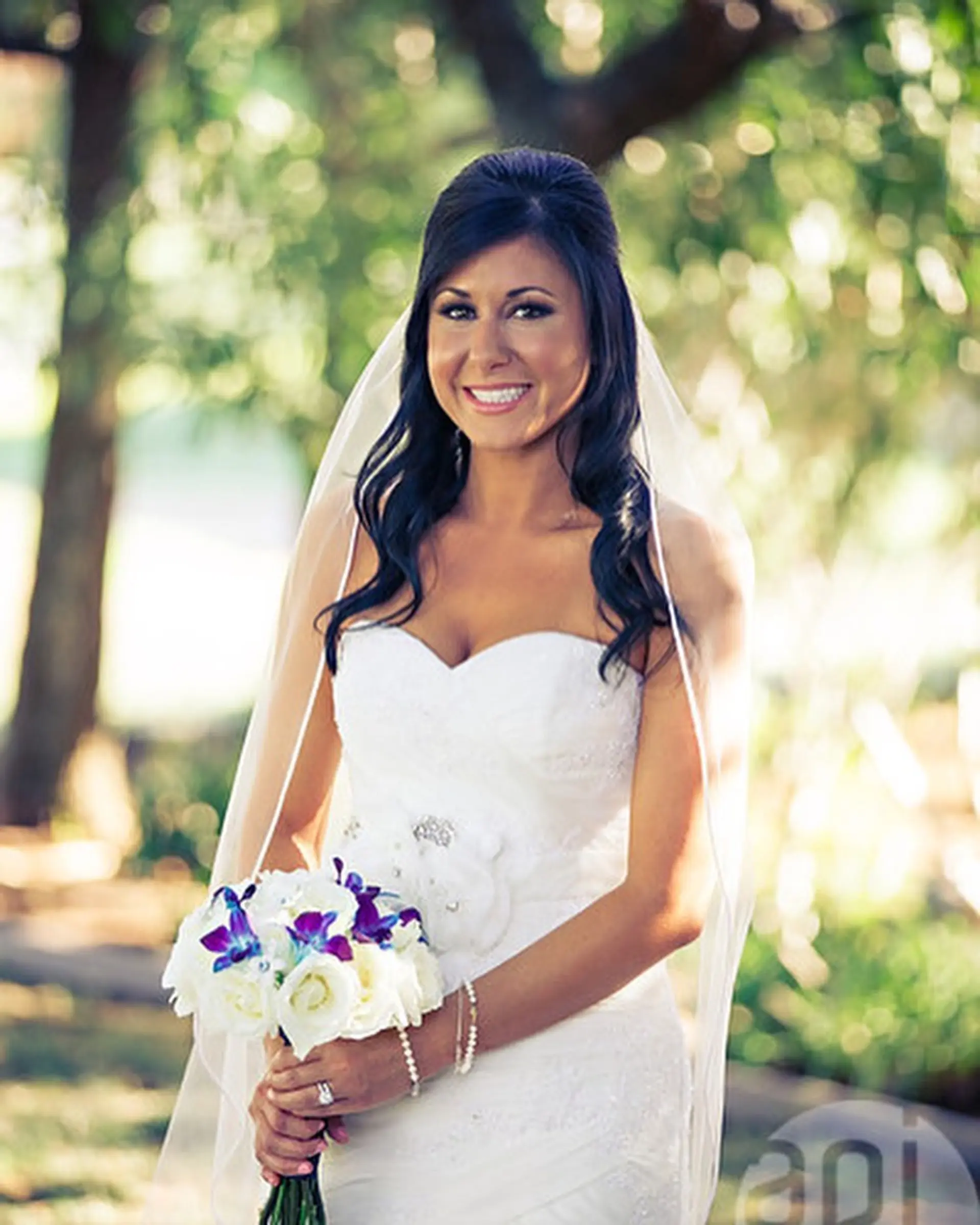 A romantic bridal half-up hairstyle featuring a lifted, voluminous crown and soft cascading curls draped over the shoulders with a wedding veil. 1