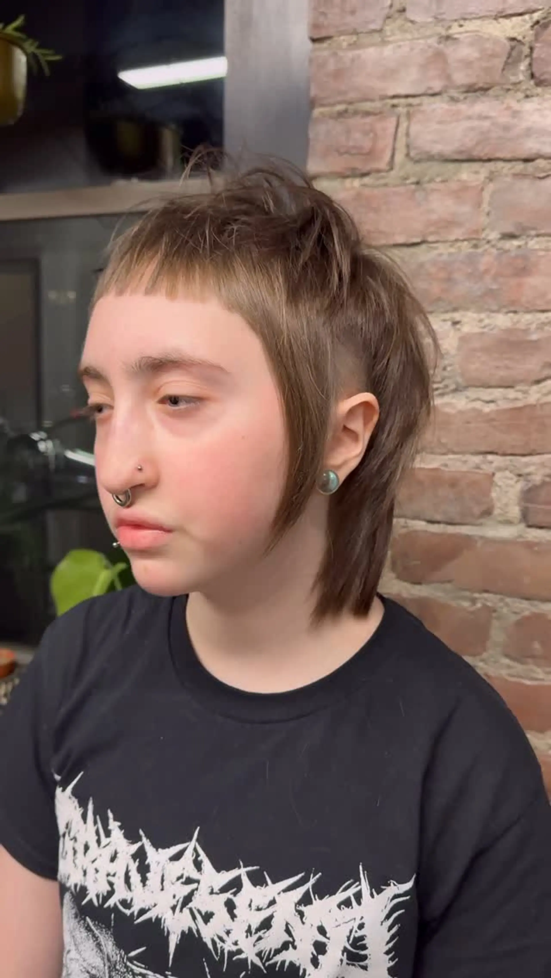 A razor-cut alternative mullet featuring blunt micro baby bangs, disconnected face-framing tendrils, an undercut side section above the ear, and textured layers throughout the crown and nape. 1