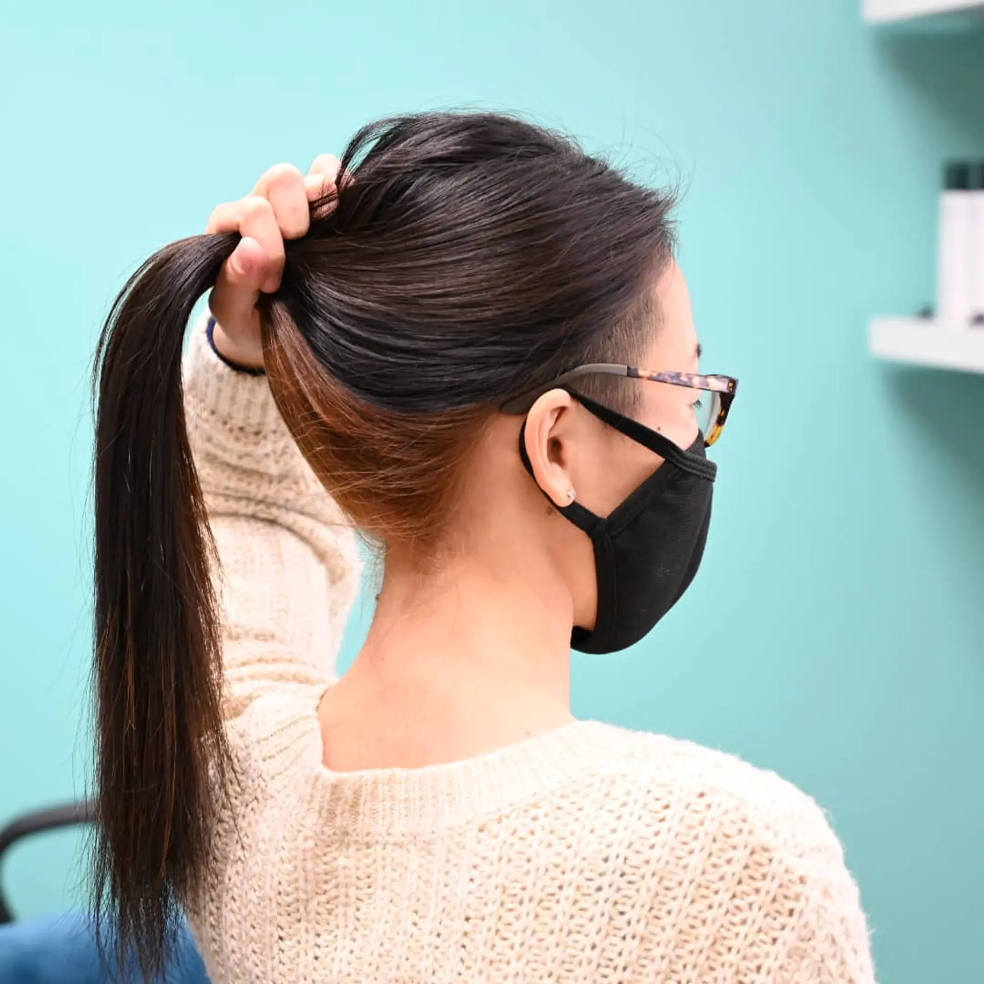 Straight dark brown hair styled upward into a ponytail to showcase hidden caramel peek-a-boo color along the nape and a shaved temple undercut. 1
