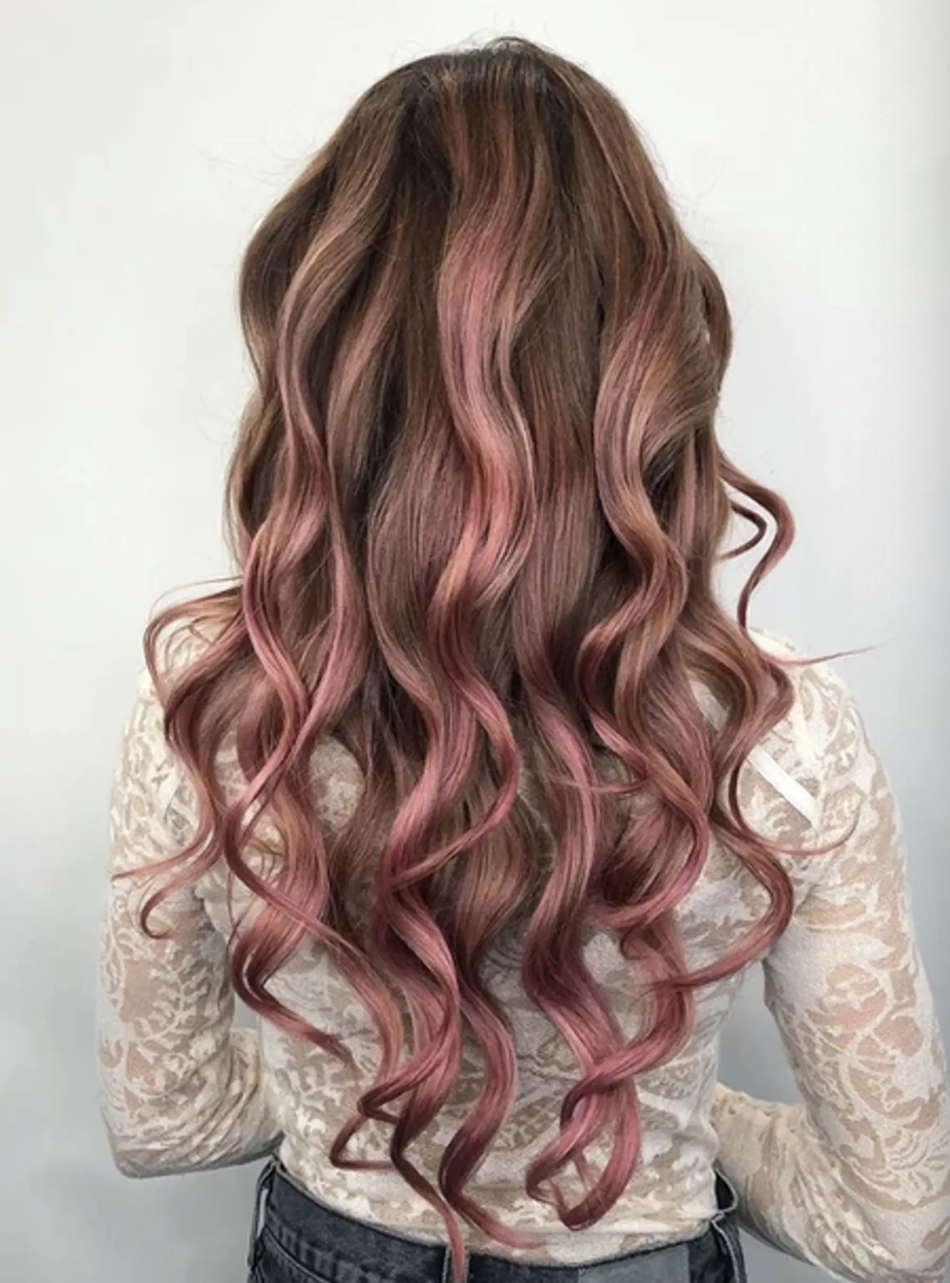 Long, wavy hair with a foliage blend of brown roots to rose gold ends, featuring loose waves and soft curls in layered style. 1