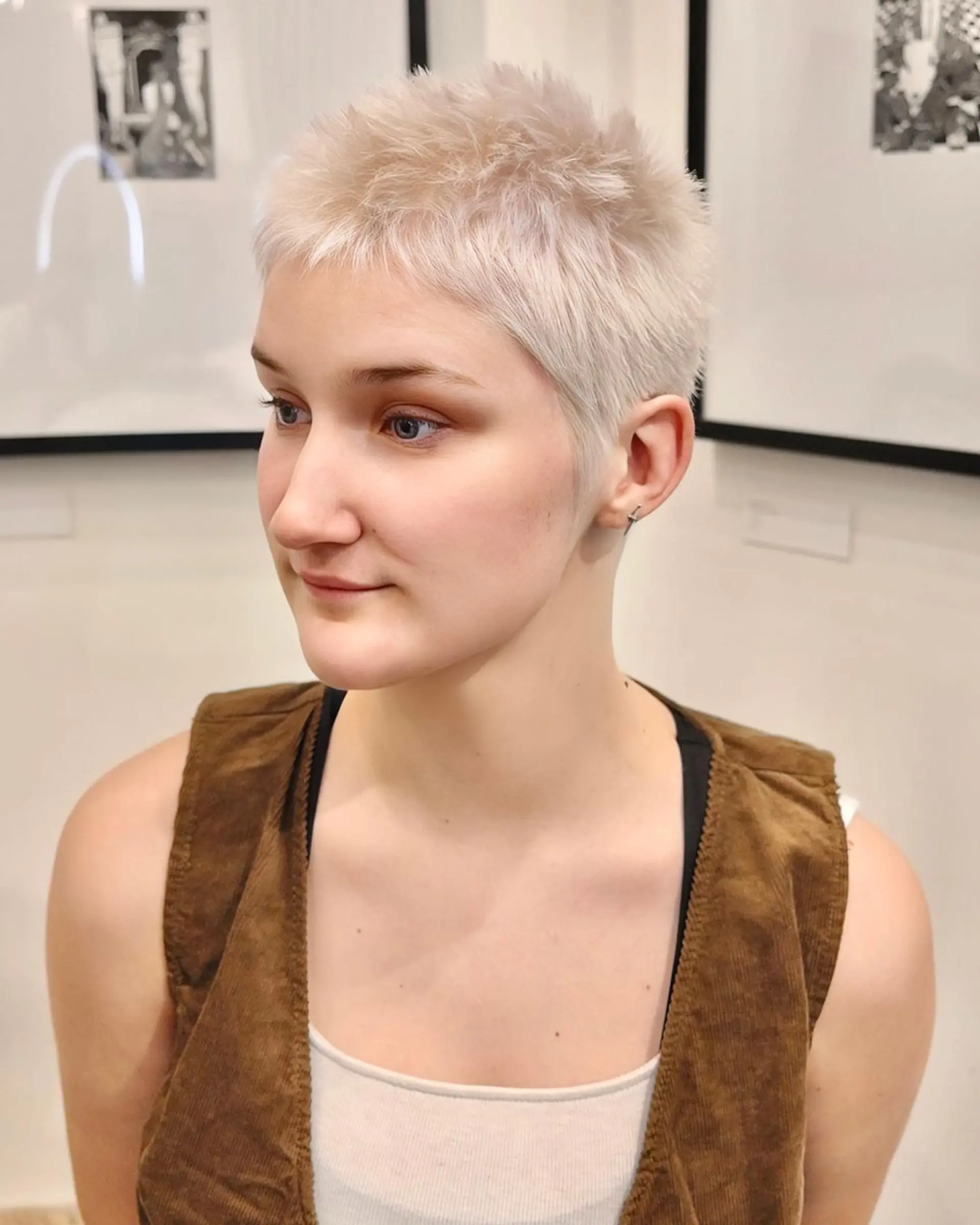 A very short, straight, platinum blonde pixie cut with neat, tight cropping and a slightly textured, feathered finish. 1