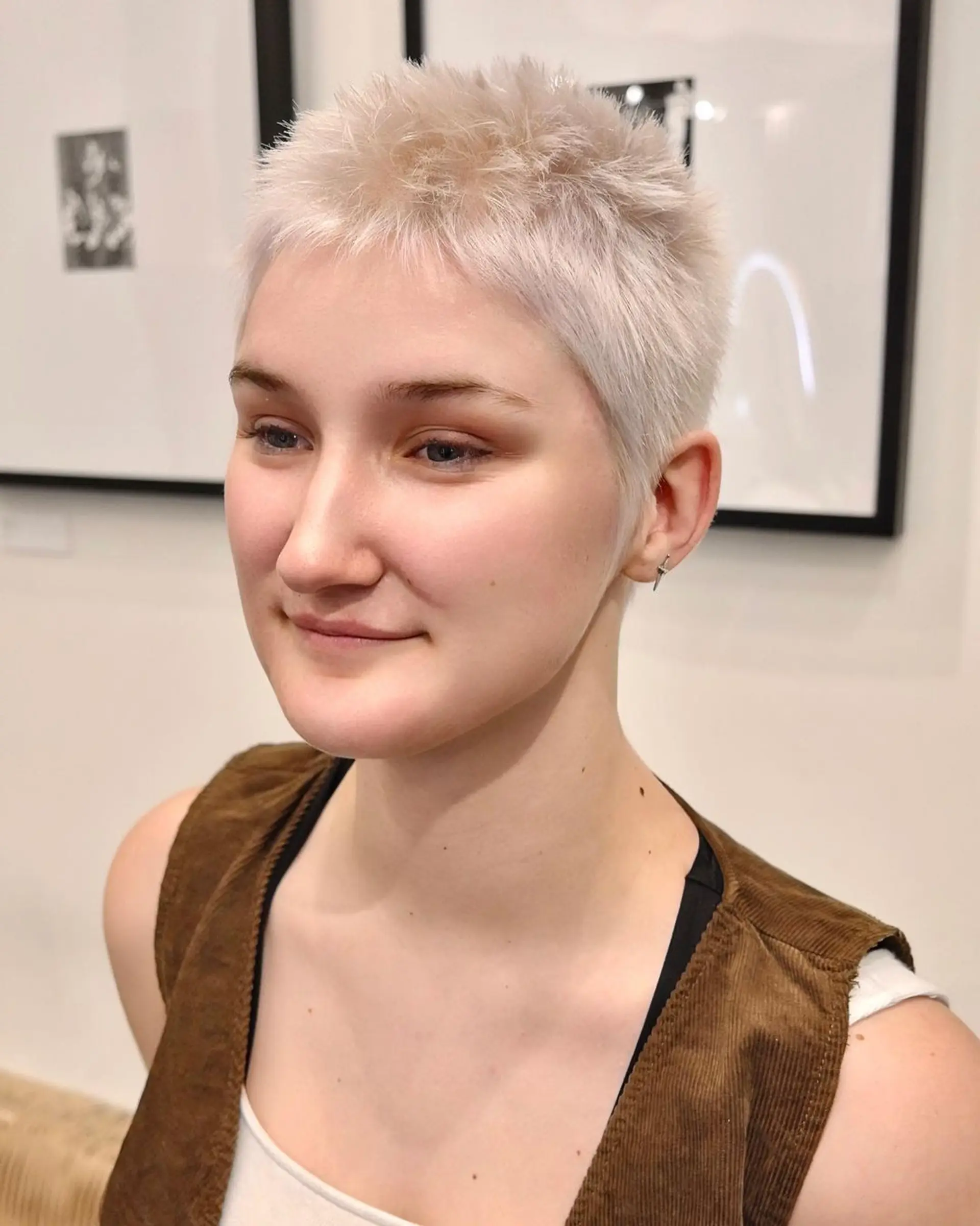 A very short, straight, platinum blonde pixie cut with neat, tight cropping and a slightly textured, feathered finish. 2