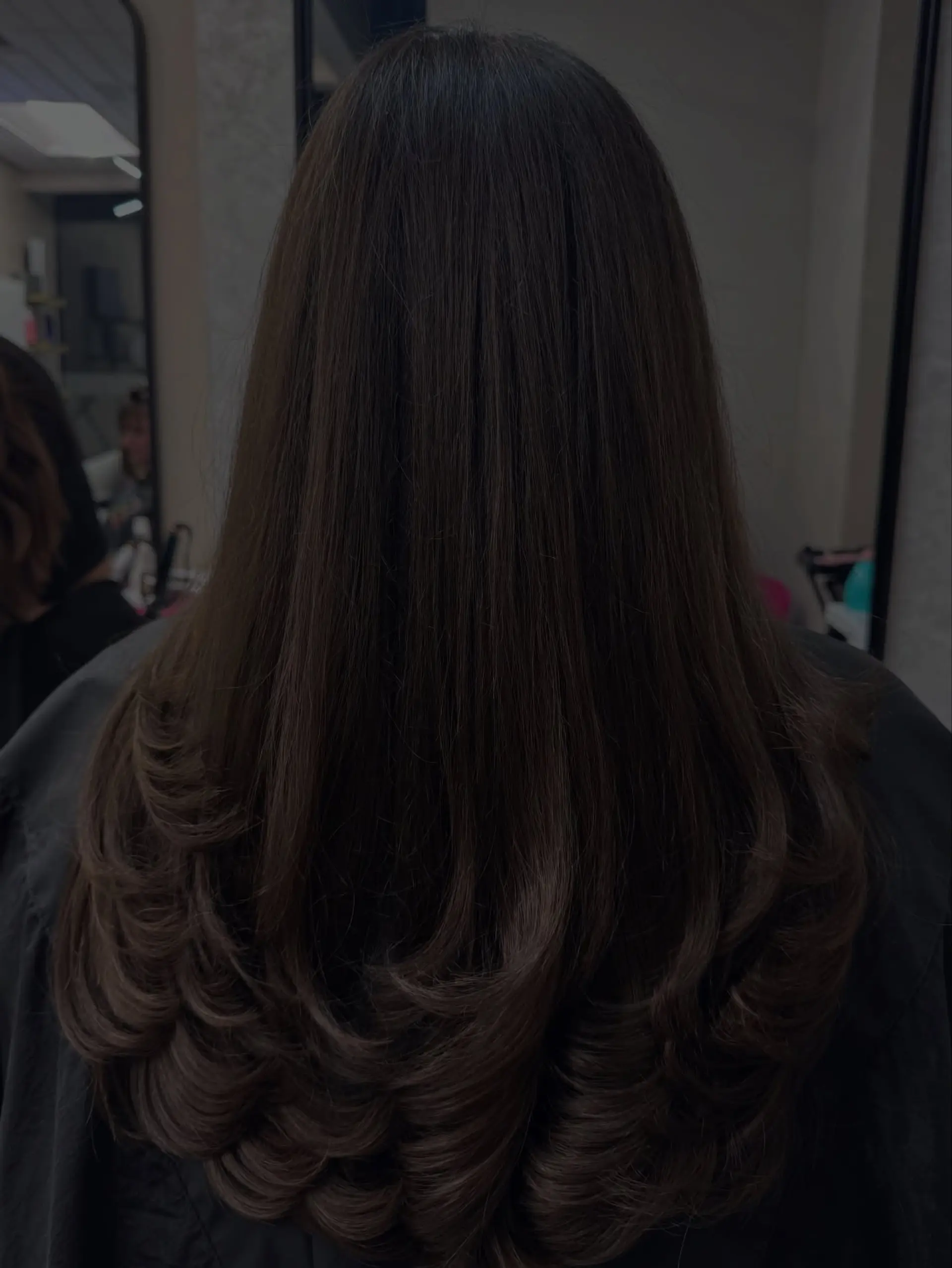 Long dark brown hair featuring defined layered tiers styled with smooth, voluminous curled-in ends. 1