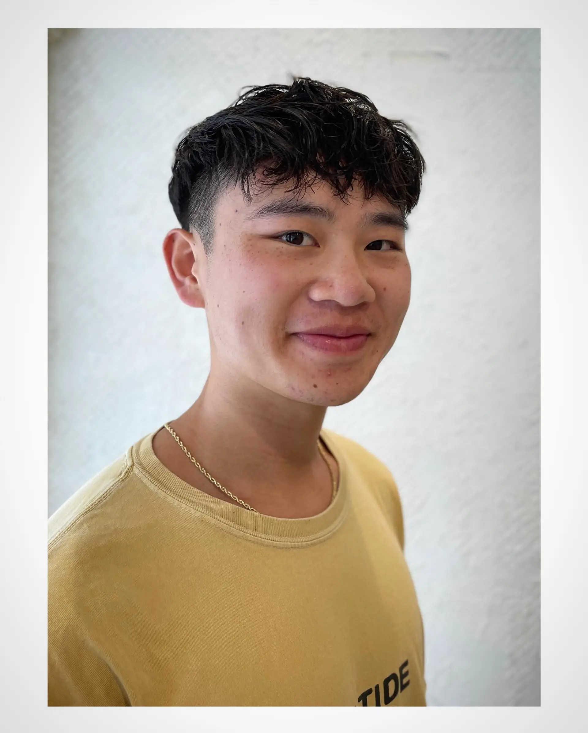 A men's short haircut featuring closely tapered undercut sides and a textured, wavy top styled forward into a piecey fringe. 1