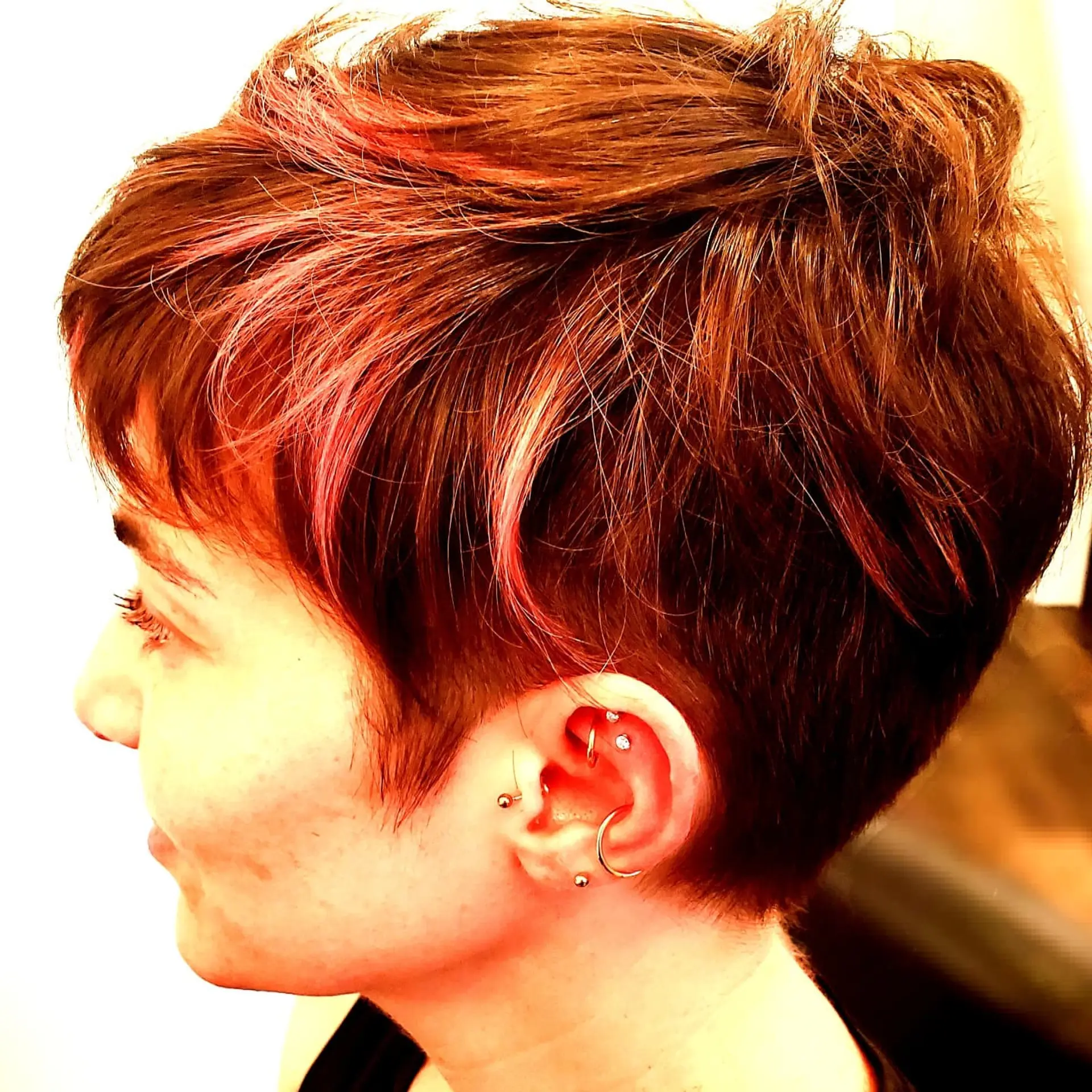 A textured short pixie cut with soft fringe and vibrant pink highlights woven into a warm brown base. 1