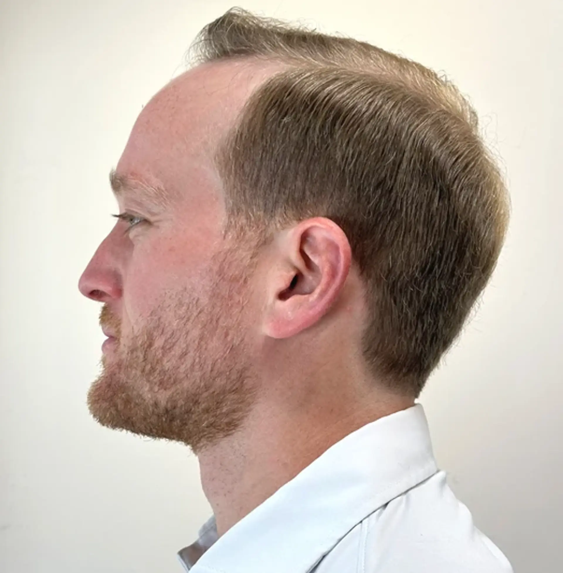 A short, straight hairstyle with a sandy blonde hue, featuring a side part, low fade, and textured top with a sleek finish. 2