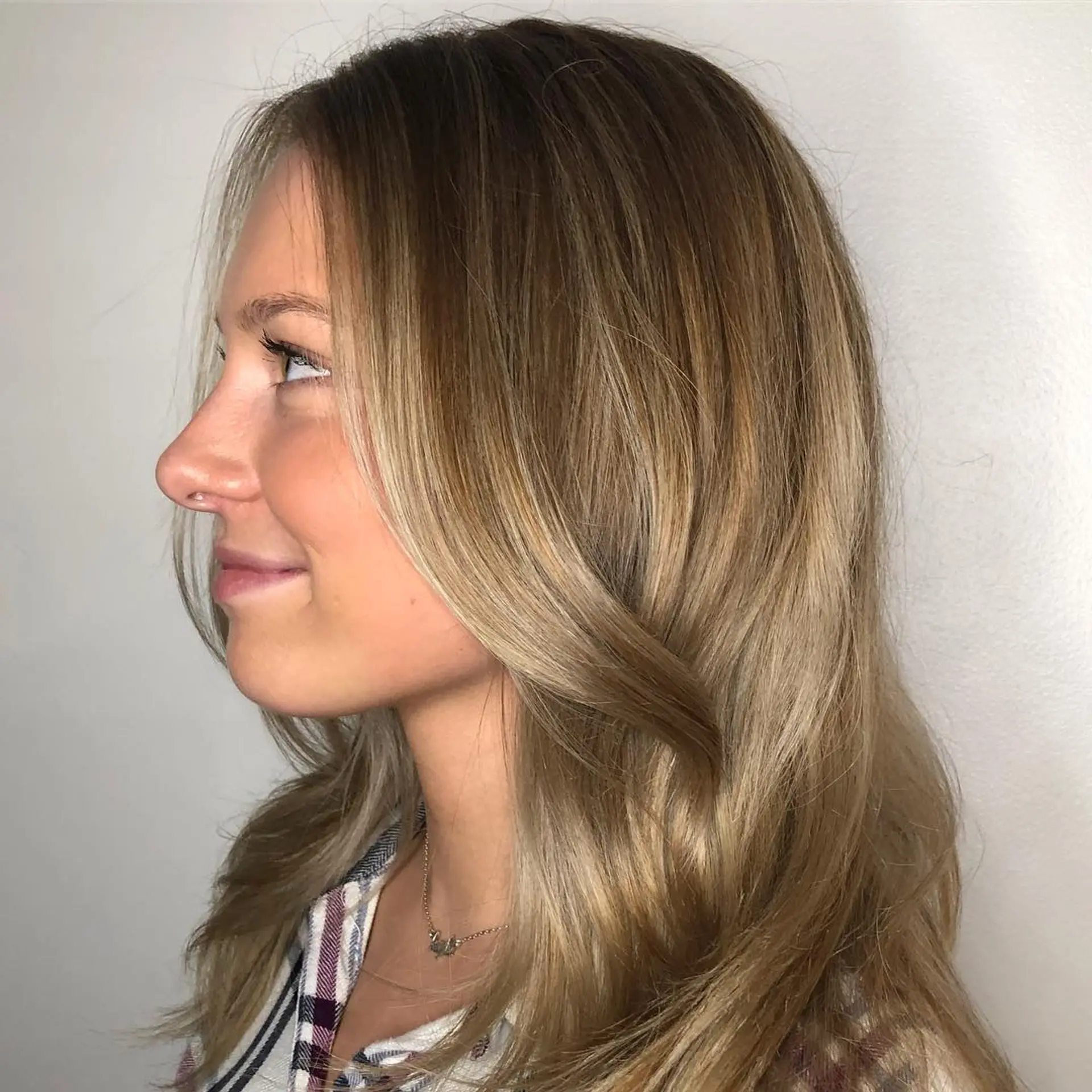 A low-maintenance lived-in blonde balayage blended over a light brunette base, styled with soft, face-framing blowout waves. 1
