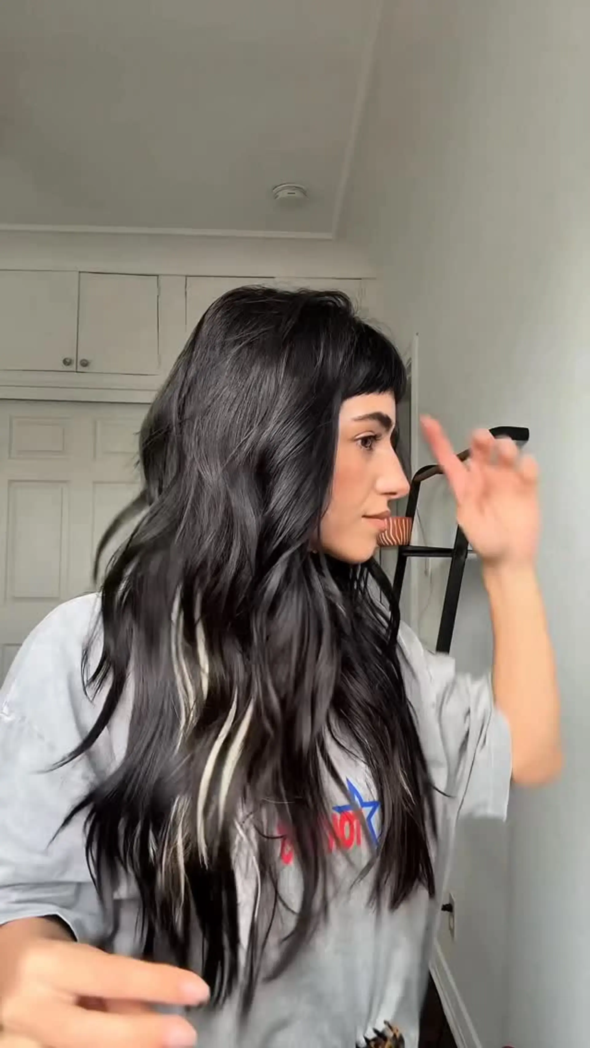 Long dark hair styled into soft, textured waves featuring blunt micro bangs and peekaboo blonde highlights. 1