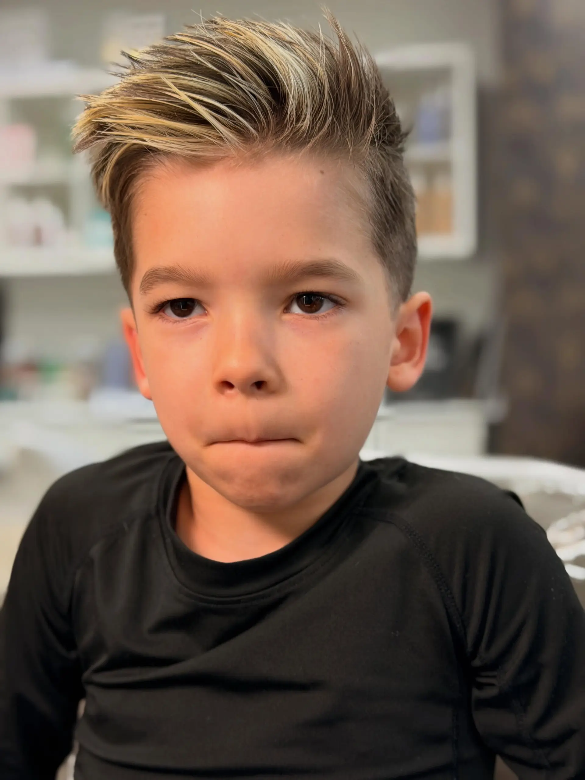 A short, modern taper cut with a textured, piecey quiff styled upwards, accented with bright blonde highlights on top. 1