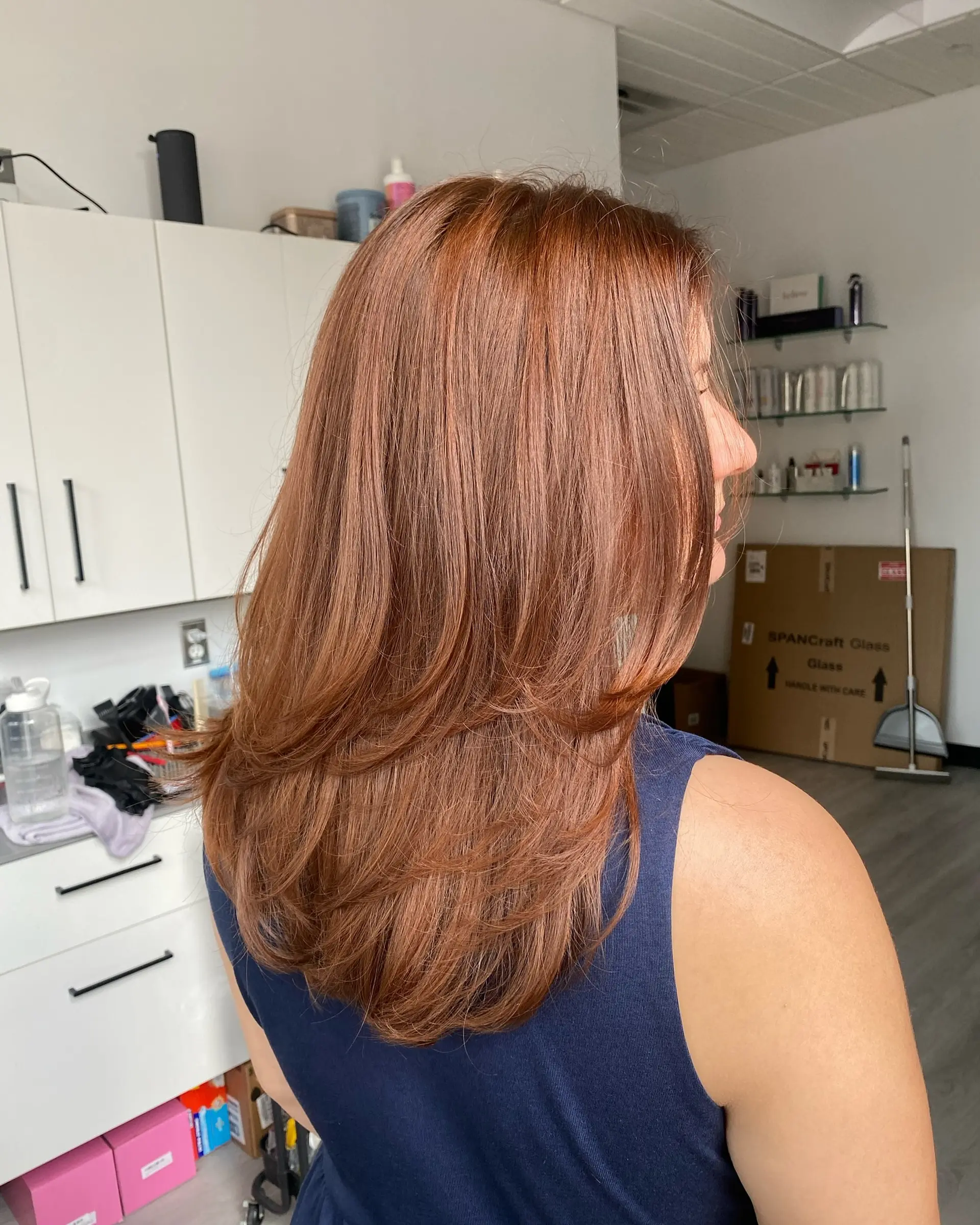 Long warm auburn hair cut with fluid, cascading layers and styled with an inward curved blowout. 1