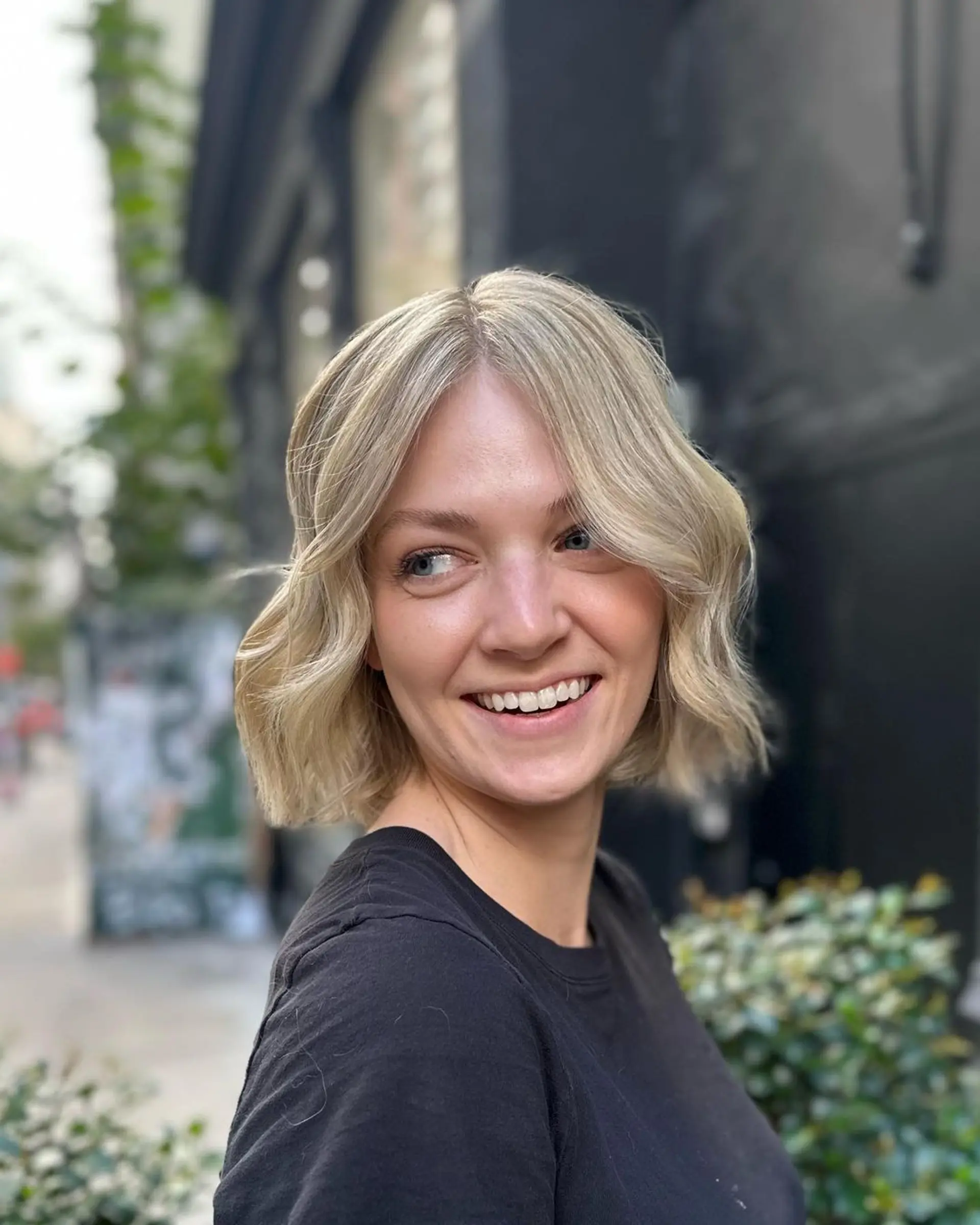 A short, wavy bob cut with platinum blonde and ash blonde hues, featuring a center part and textured ends for a soft, voluminous look.

Color by @simabeautynyc
Cut and style by @juliamannino_hair 3