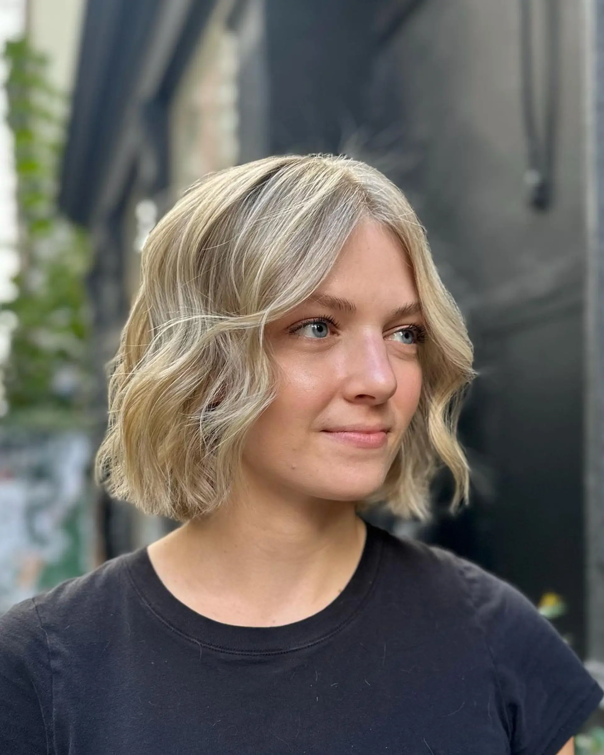 A short, wavy bob cut with platinum blonde and ash blonde hues, featuring a center part and textured ends for a soft, voluminous look.

Color by @simabeautynyc
Cut and style by @juliamannino_hair 1