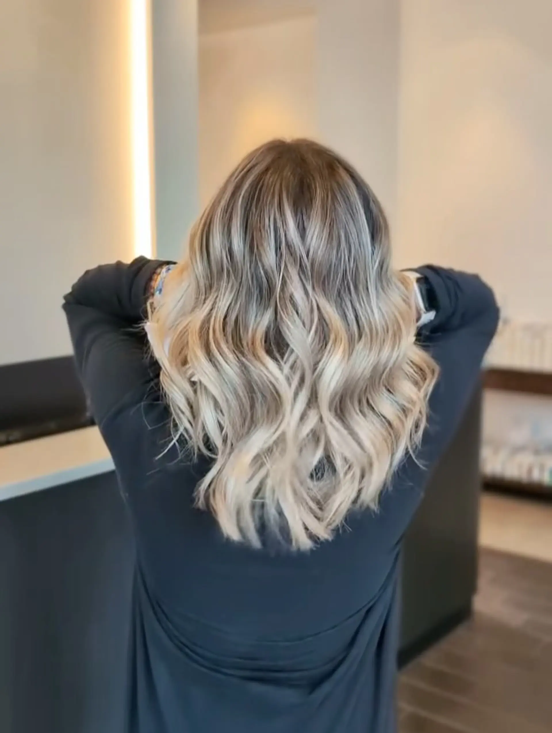 Medium-length ash blonde foilyage styled in soft, textured waves with a natural shadow root. 1