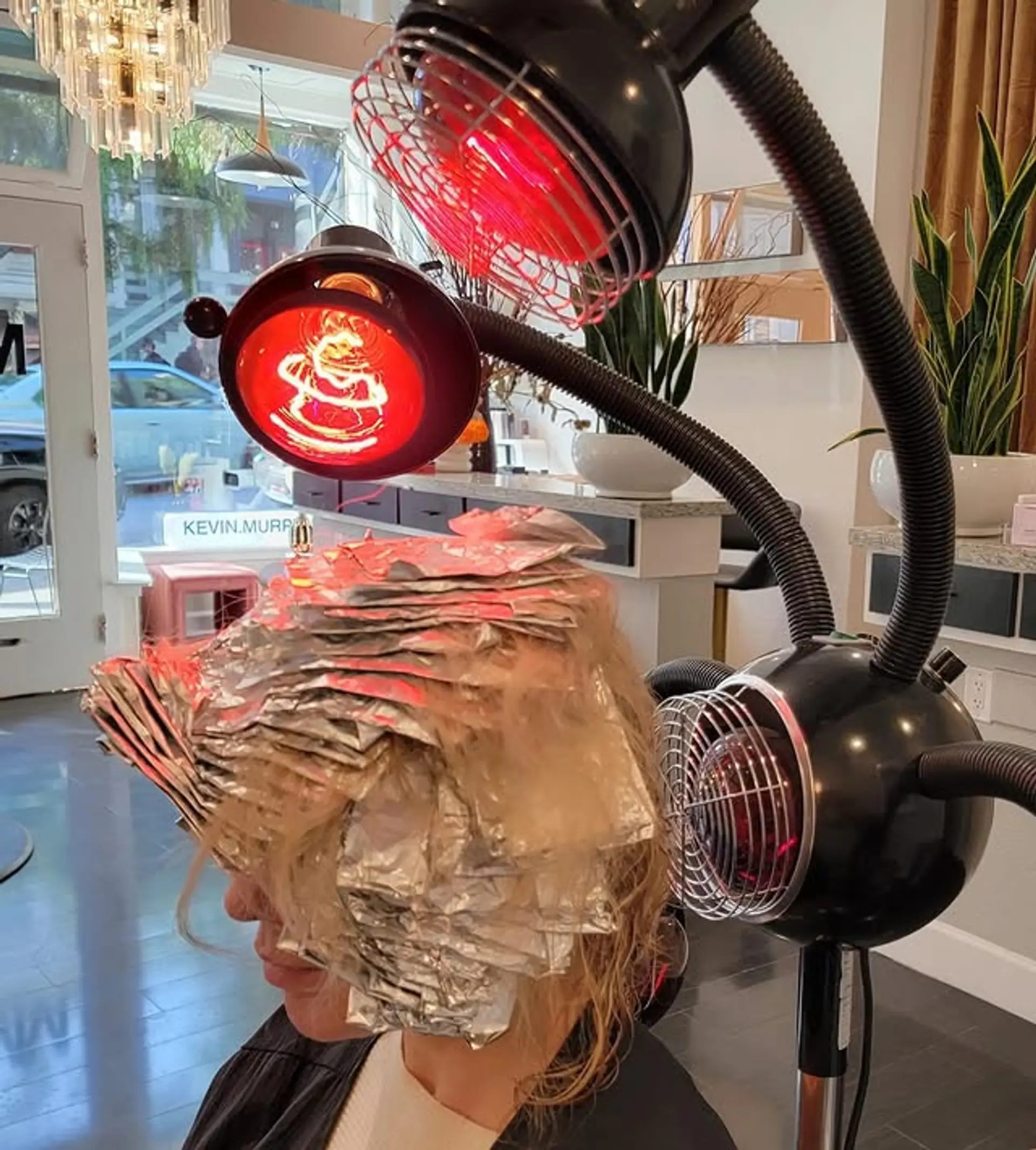 The hairstyle is currently a work in progress, featuring numerous foil packets meticulously placed throughout medium-length hair, suggesting a full head of highlights or a significant blonde color service to lighten the hair. 1