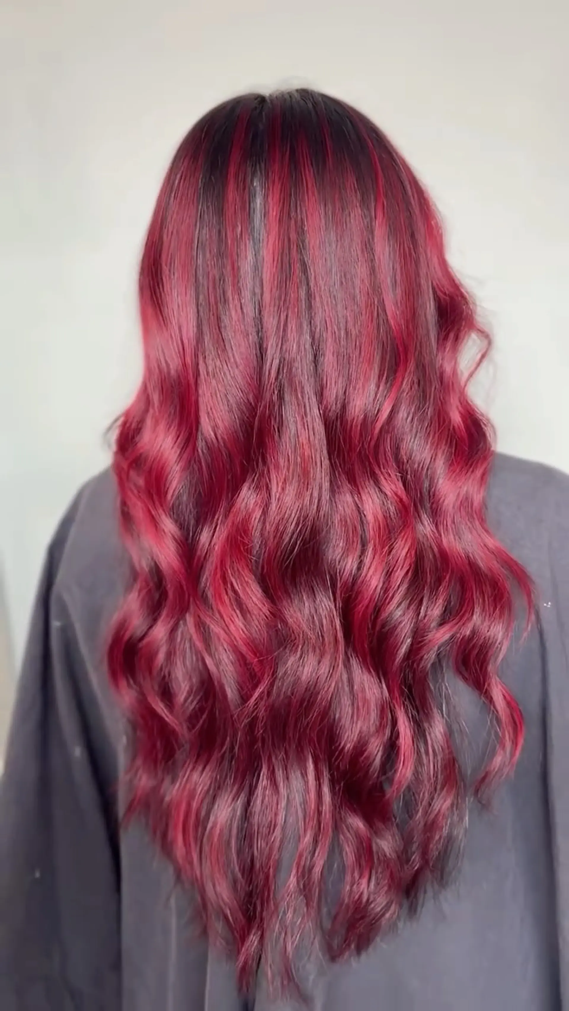 Long hair styled in soft, loose waves featuring a vivid crimson balayage over deep brunette roots. 1