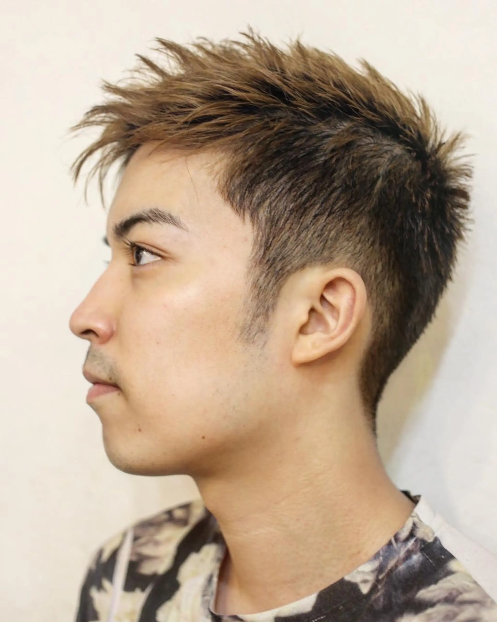 This hairstyle features short, straight hair with an undercut on the sides and back. The top is styled with textured, light brown spikes, adding a modern, edgy look.