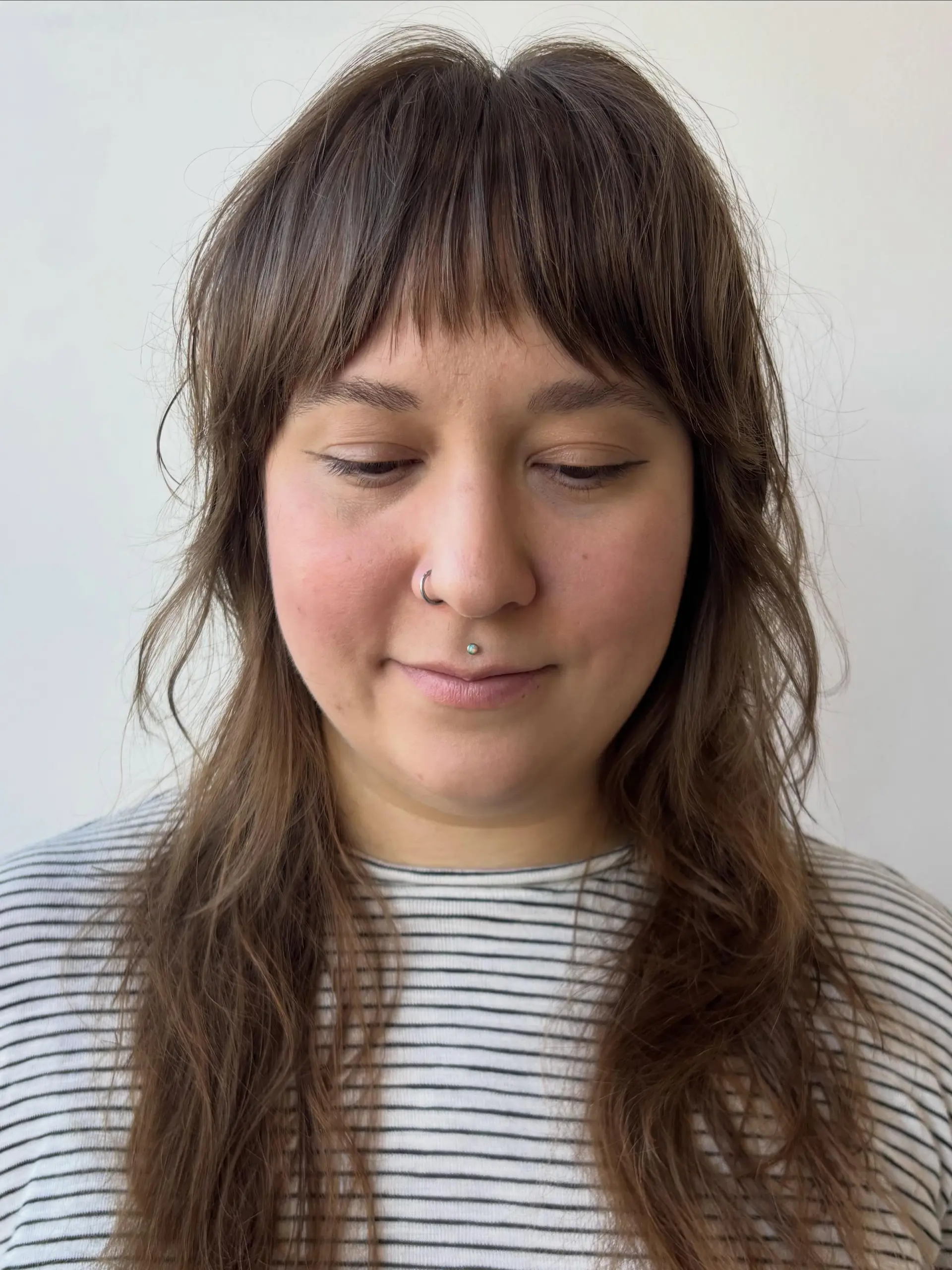 A long textured brunette shag haircut with wispy straight fringe and feathered face-framing layers. 1