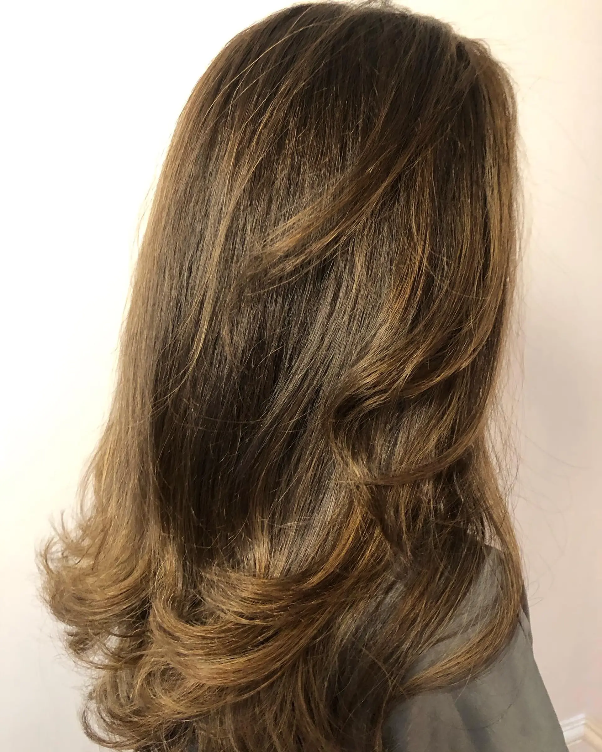 Long layered brunette hair styled with a voluminous blowout featuring curled, flipped ends and subtle dimensional highlights. 1