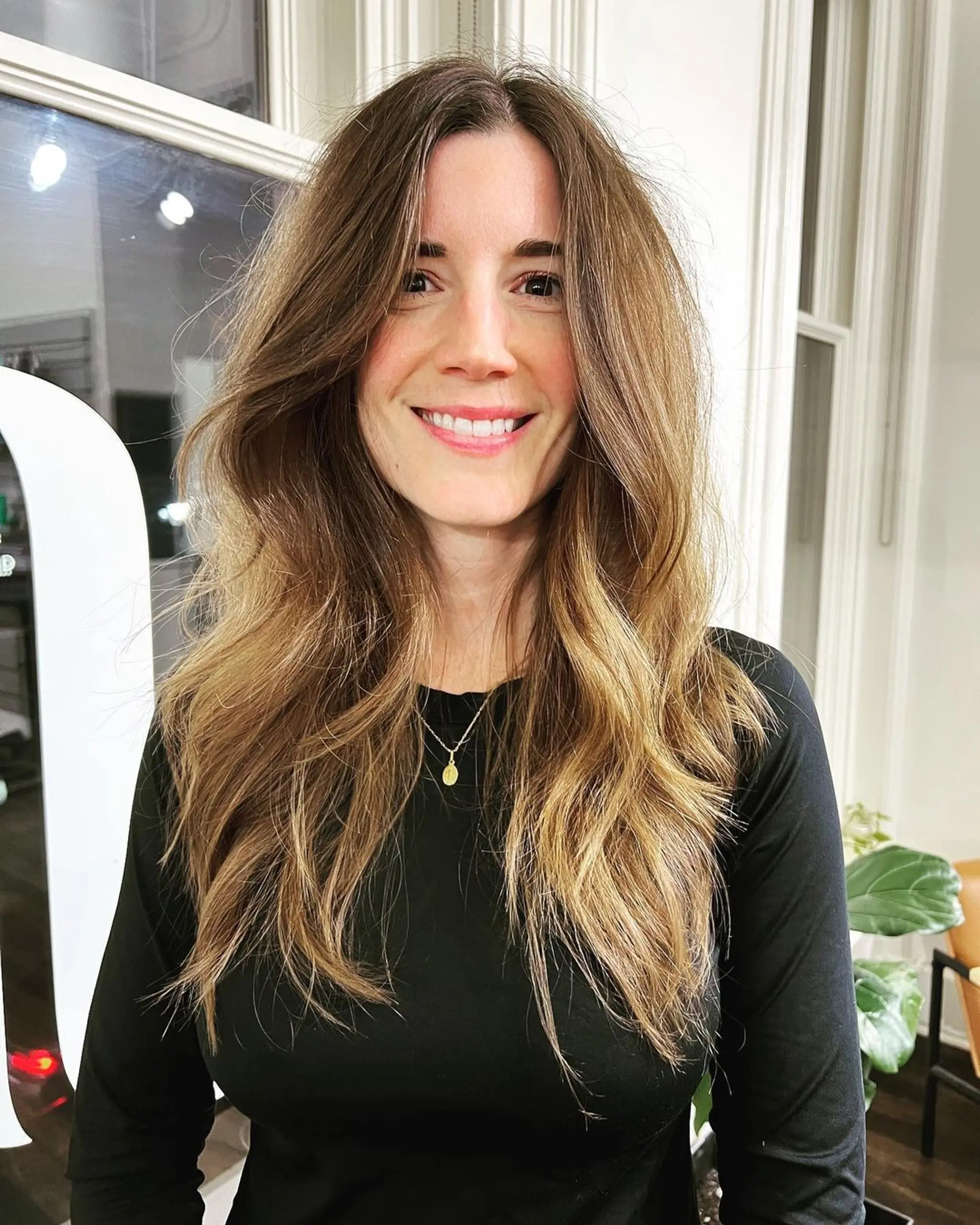 Long, wavy light brown hair with blonde highlights, featuring loose waves, face-framing layers, a middle part, and subtle ombre from darker roots to lighter ends.