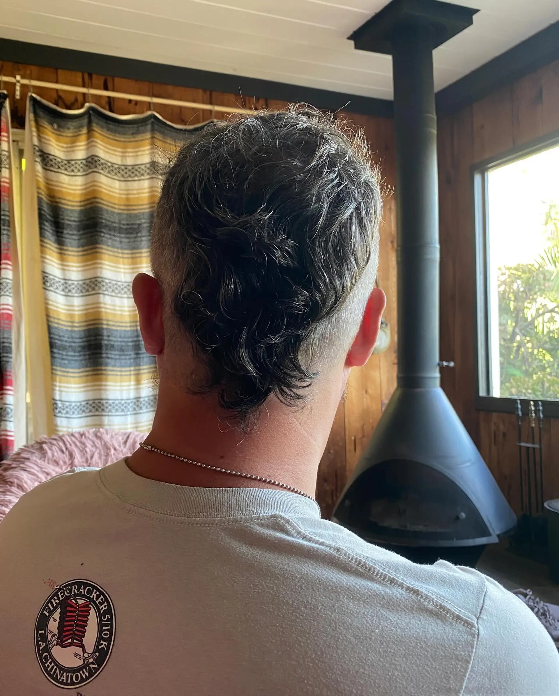 A modern short mohawk-mullet featuring close-clipped shaved sides and natural wavy texture running along the center down the nape. 1