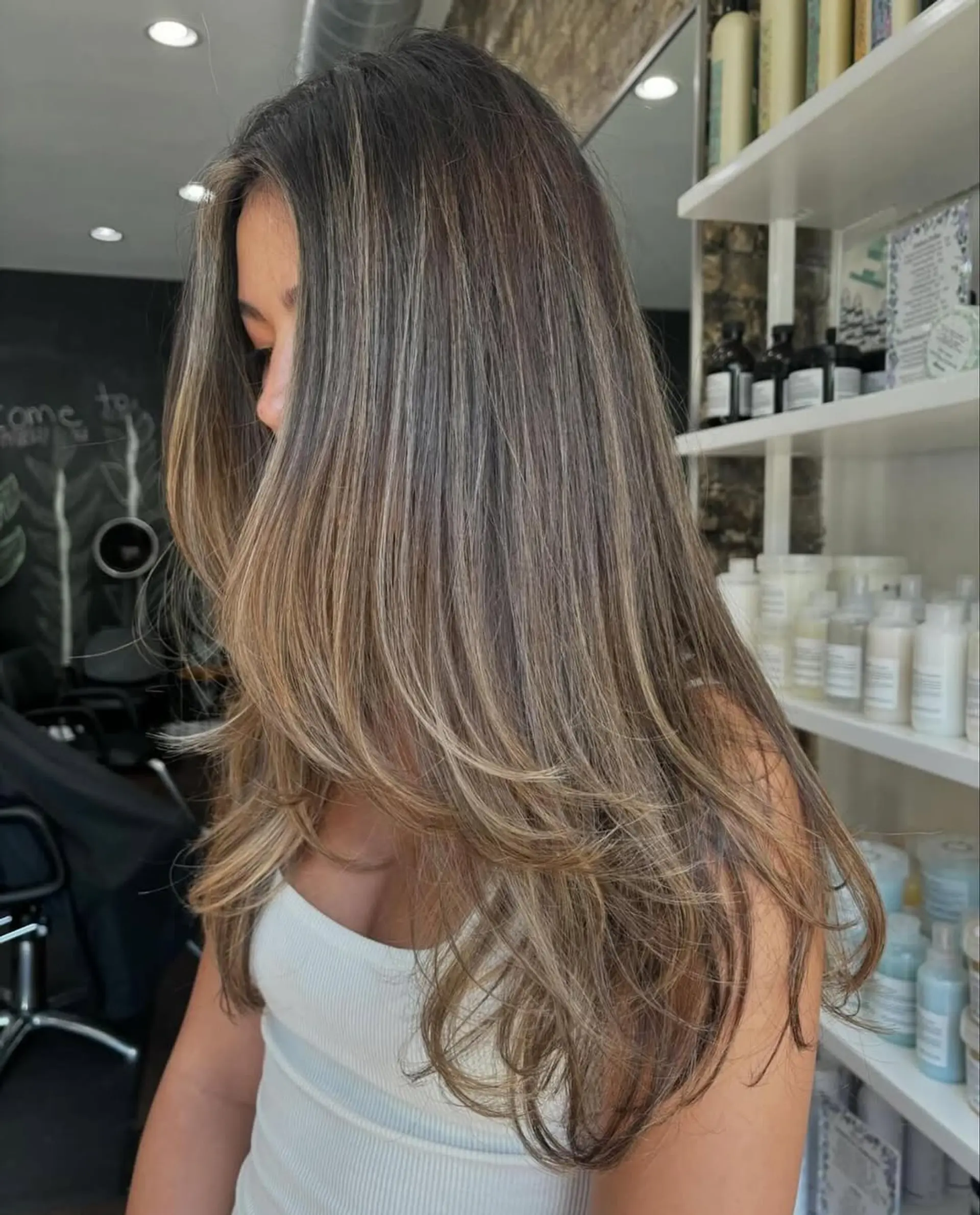 A stunning long, layered hairstyle featuring bronde balayage with seamless face-framing layers and soft, voluminous waves for a chic, dimensional look. 2