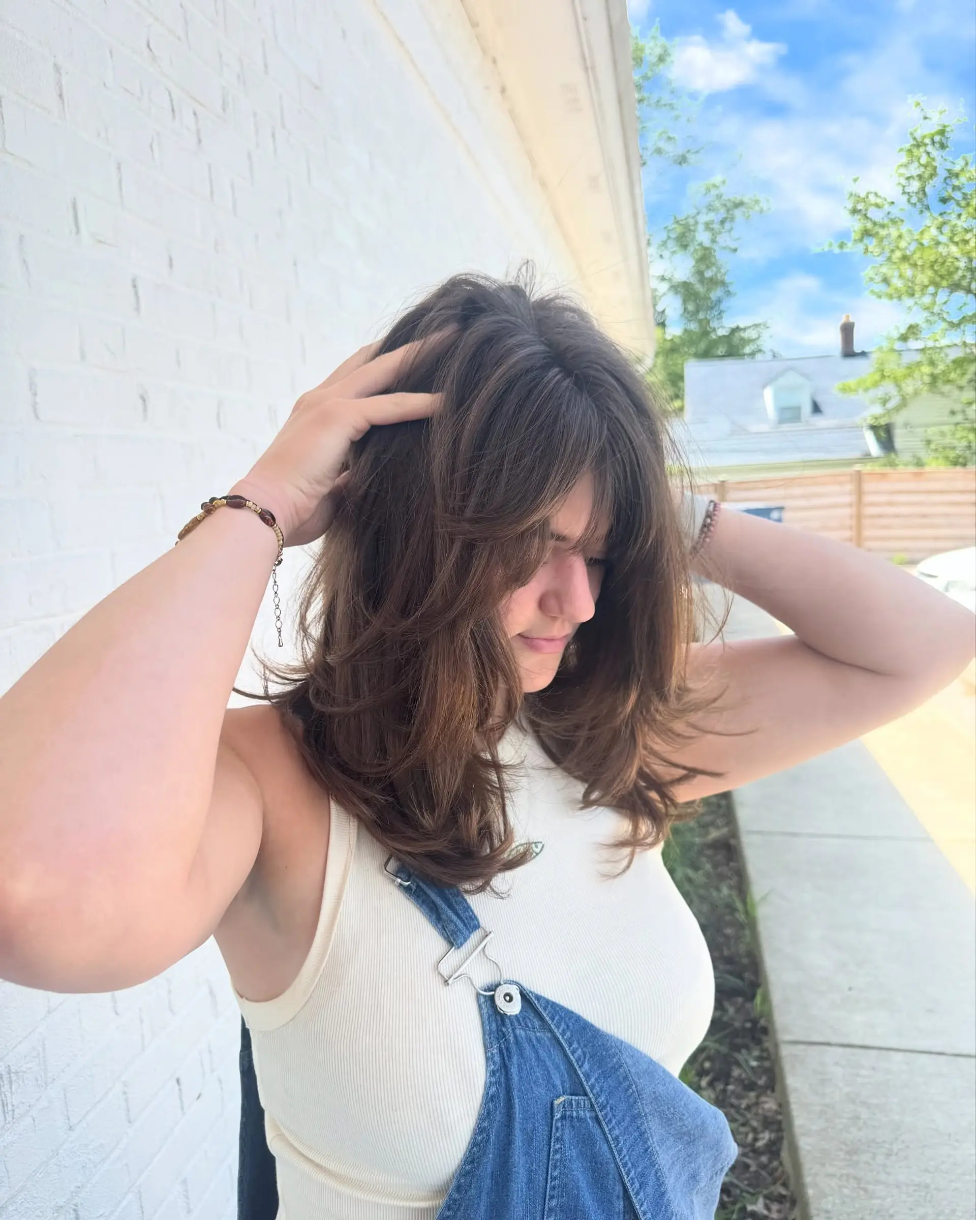 A mid-length textured brunette haircut featuring soft face-framing layers and wispy curtain bangs. 1