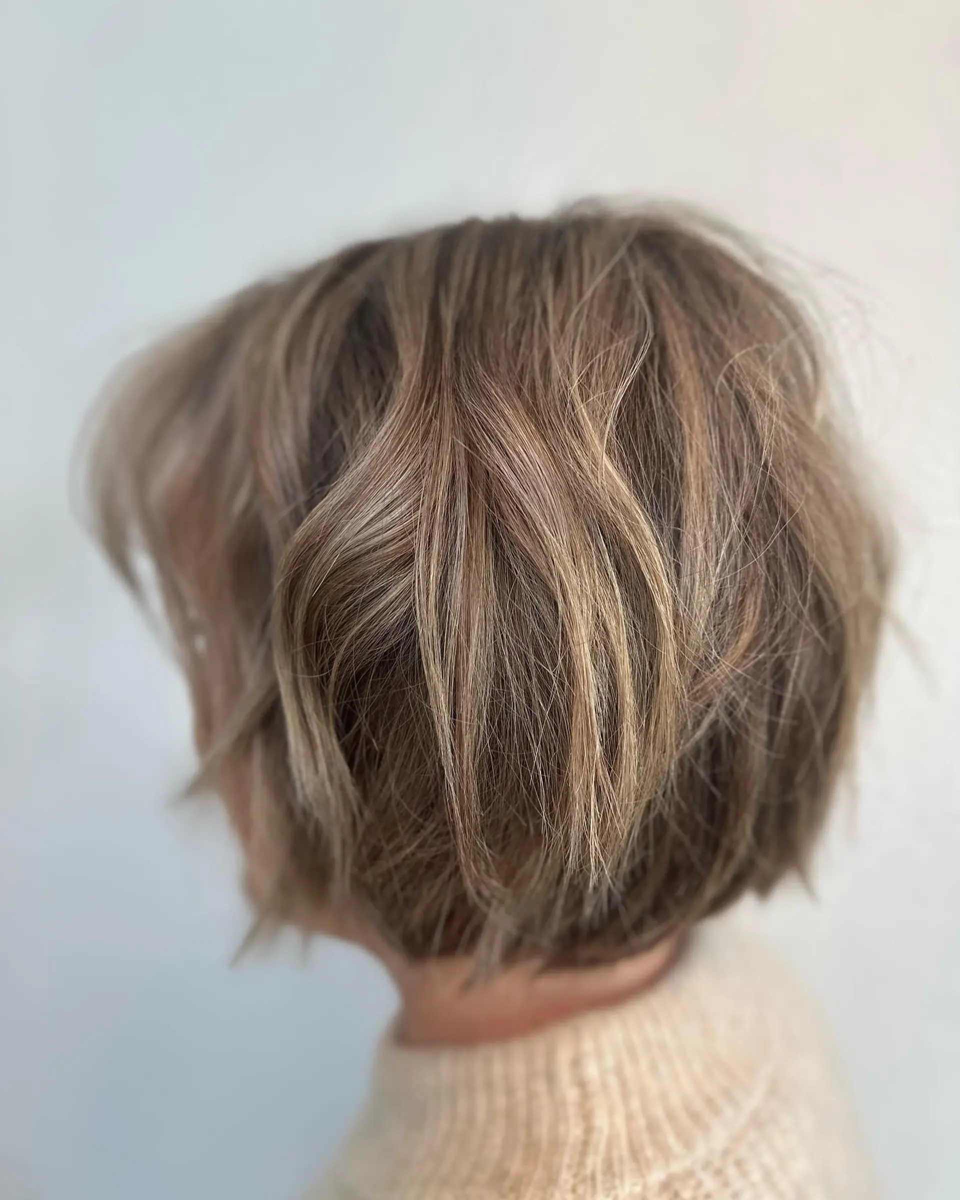 A textured short graduated bob haircut featuring subtle layering and dimensional blonde highlights. 1