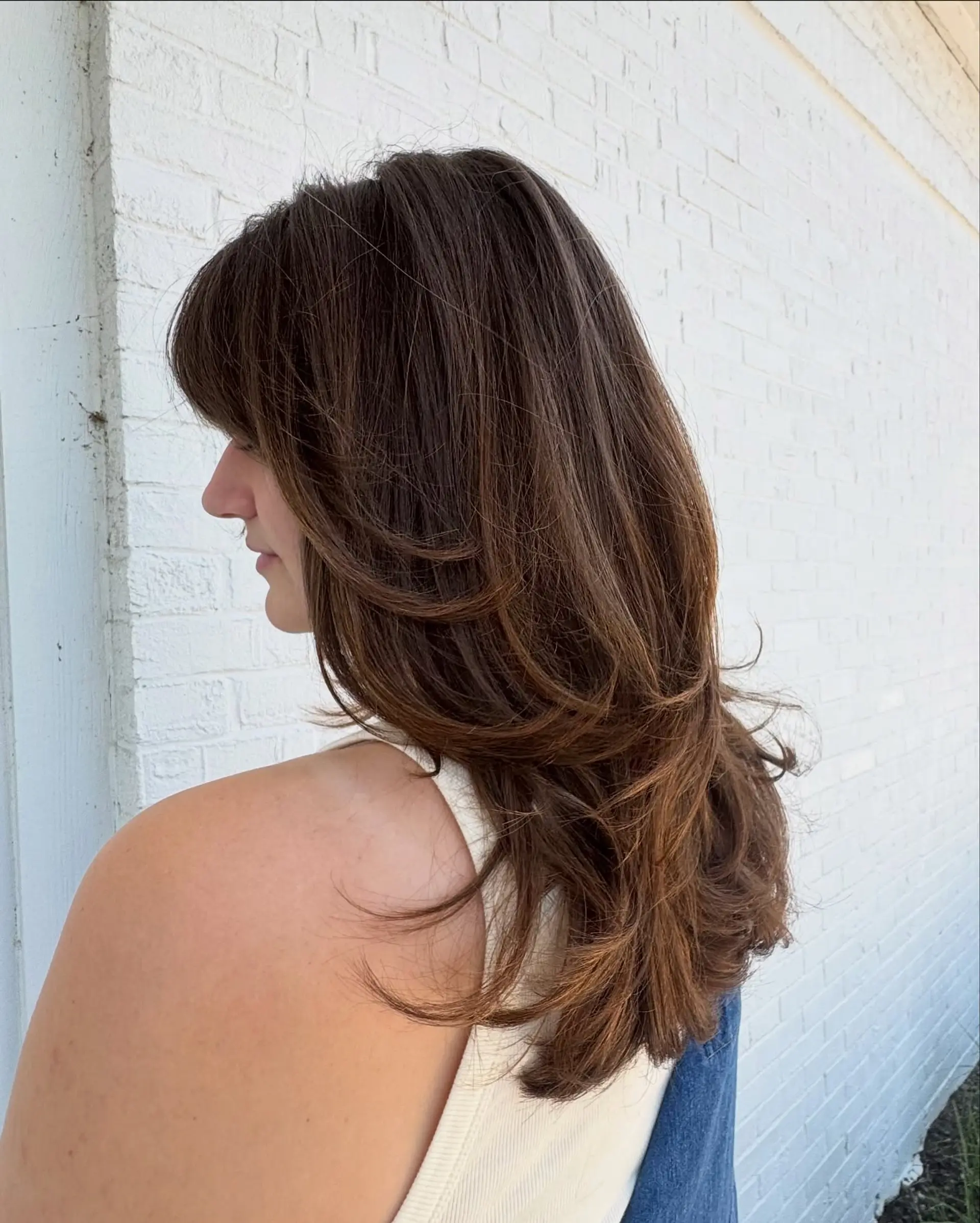 A long brunette haircut featuring soft feathered layers, face-framing pieces, and flipped ends styled with a smooth blowout. 1