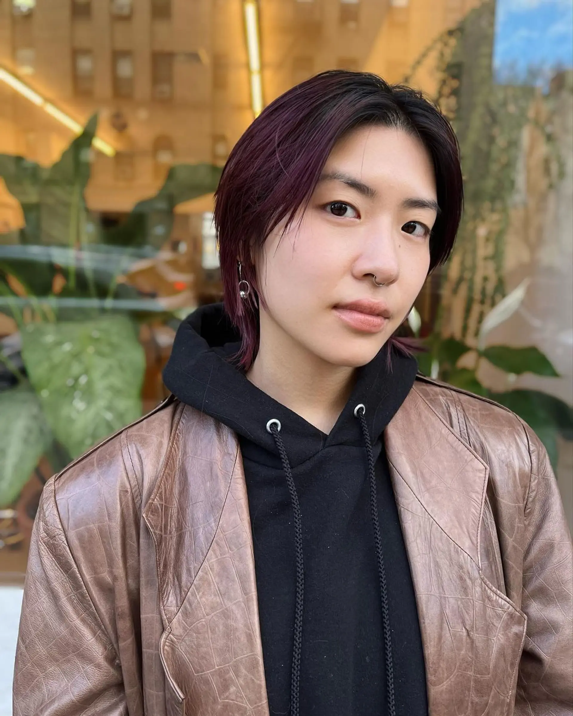 A chic and edgy short hairstyle with a layered cut that falls to ear-length, featuring side-swept bangs. The hair color is dark brown with vibrant plum highlights. 2