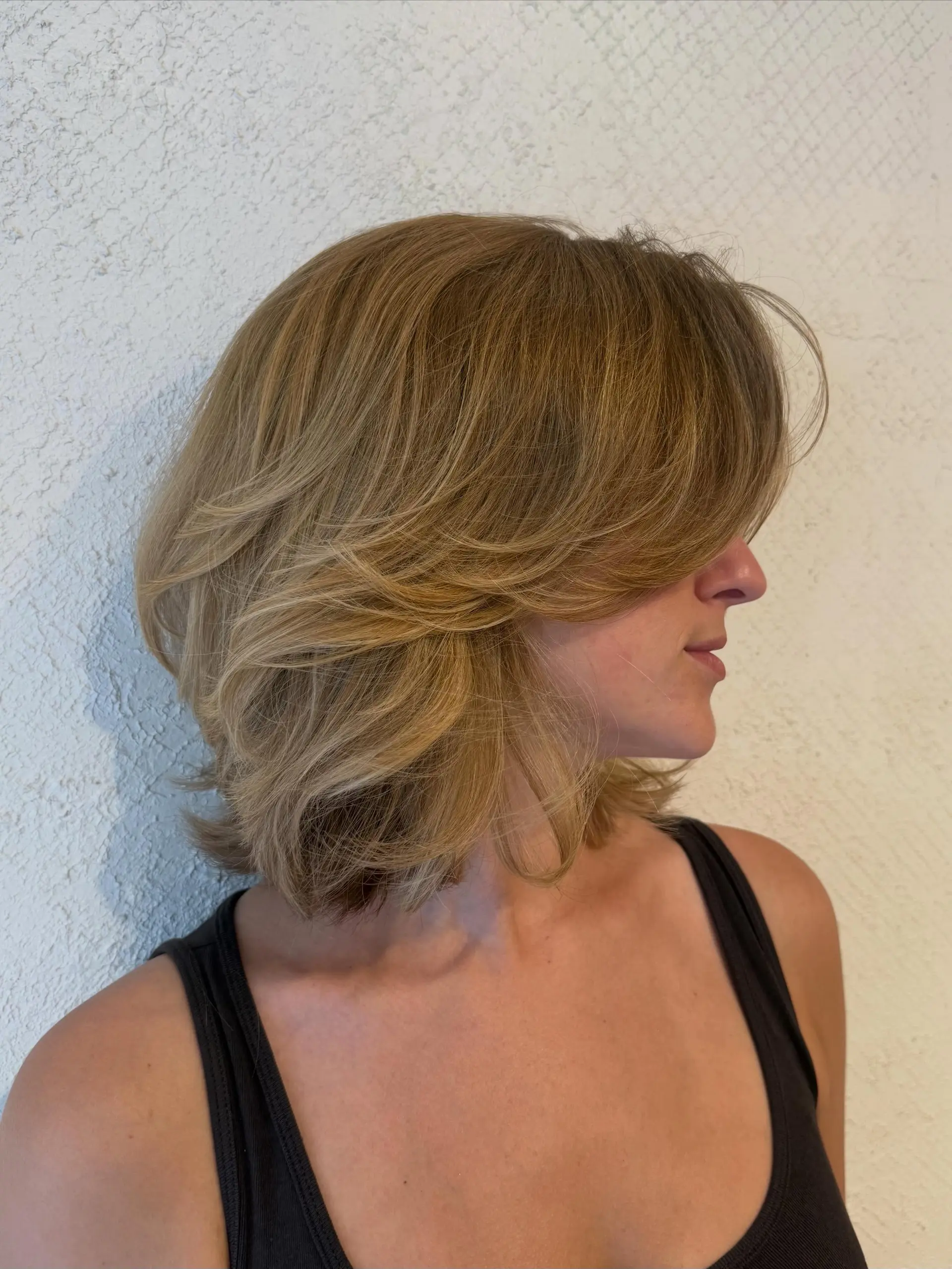 A textured, shoulder-grazing bob featuring soft, feathered layers and sweeping curtain bangs styled with bouncy volume. 1