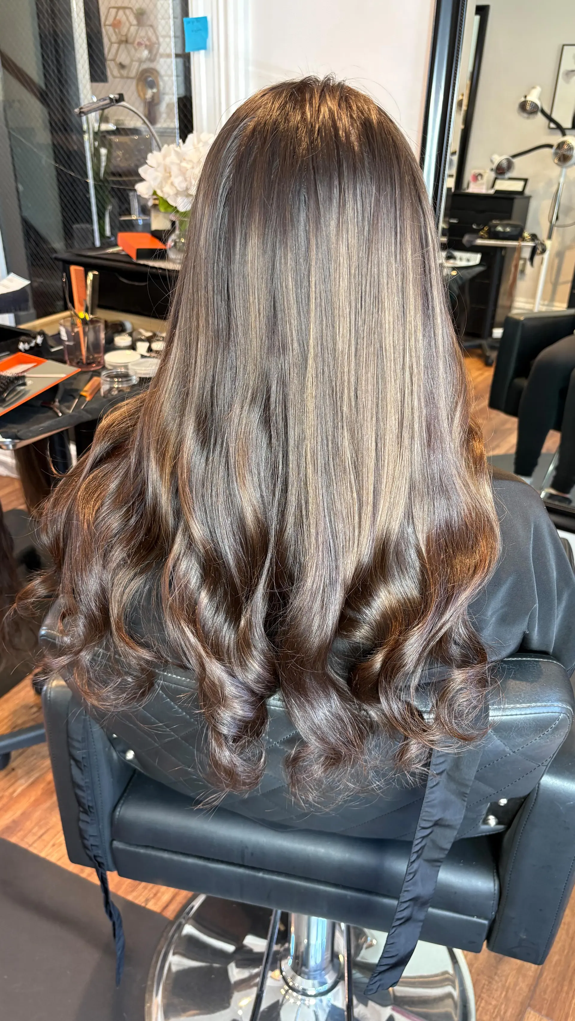 Long brown hair with subtle warm highlights, smoothed straight through the crown and styled with soft, defined curls at the ends. 1