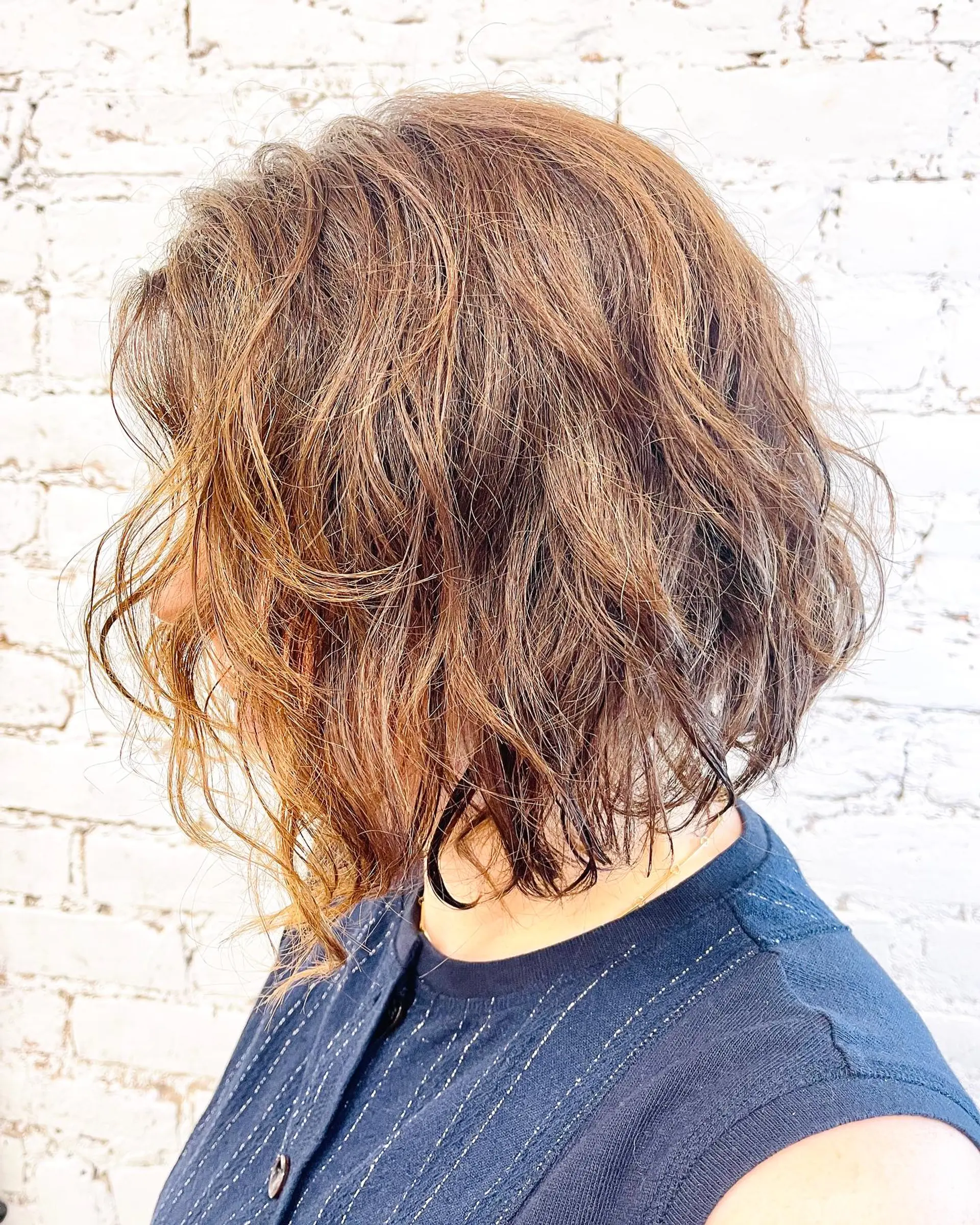 A textured chin-to-neck length wavy bob featuring warm brown tones and piecey, lived-in layers. 1