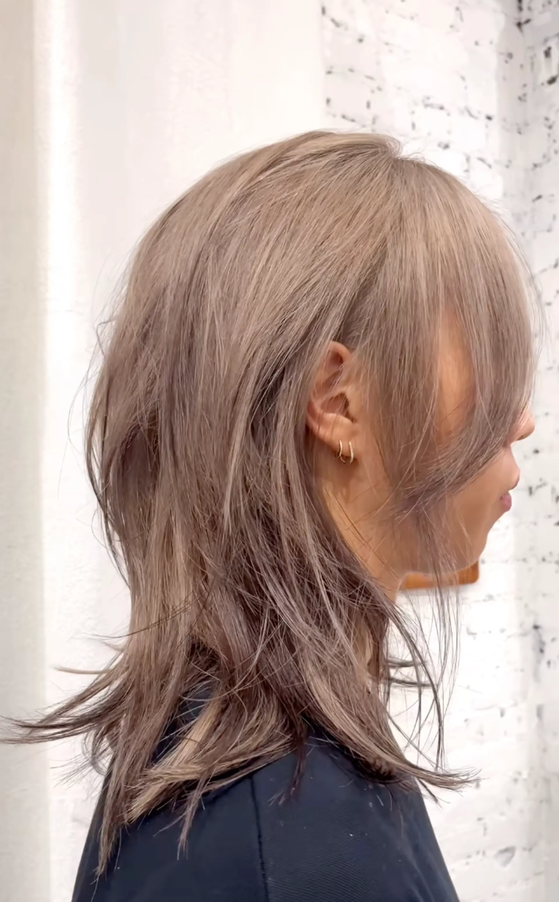 A captivating Ethereal Layer Cascade with a rich ash brown base, silvery blonde highlights, layered and feathered ends, and soft side-swept bangs. 1
