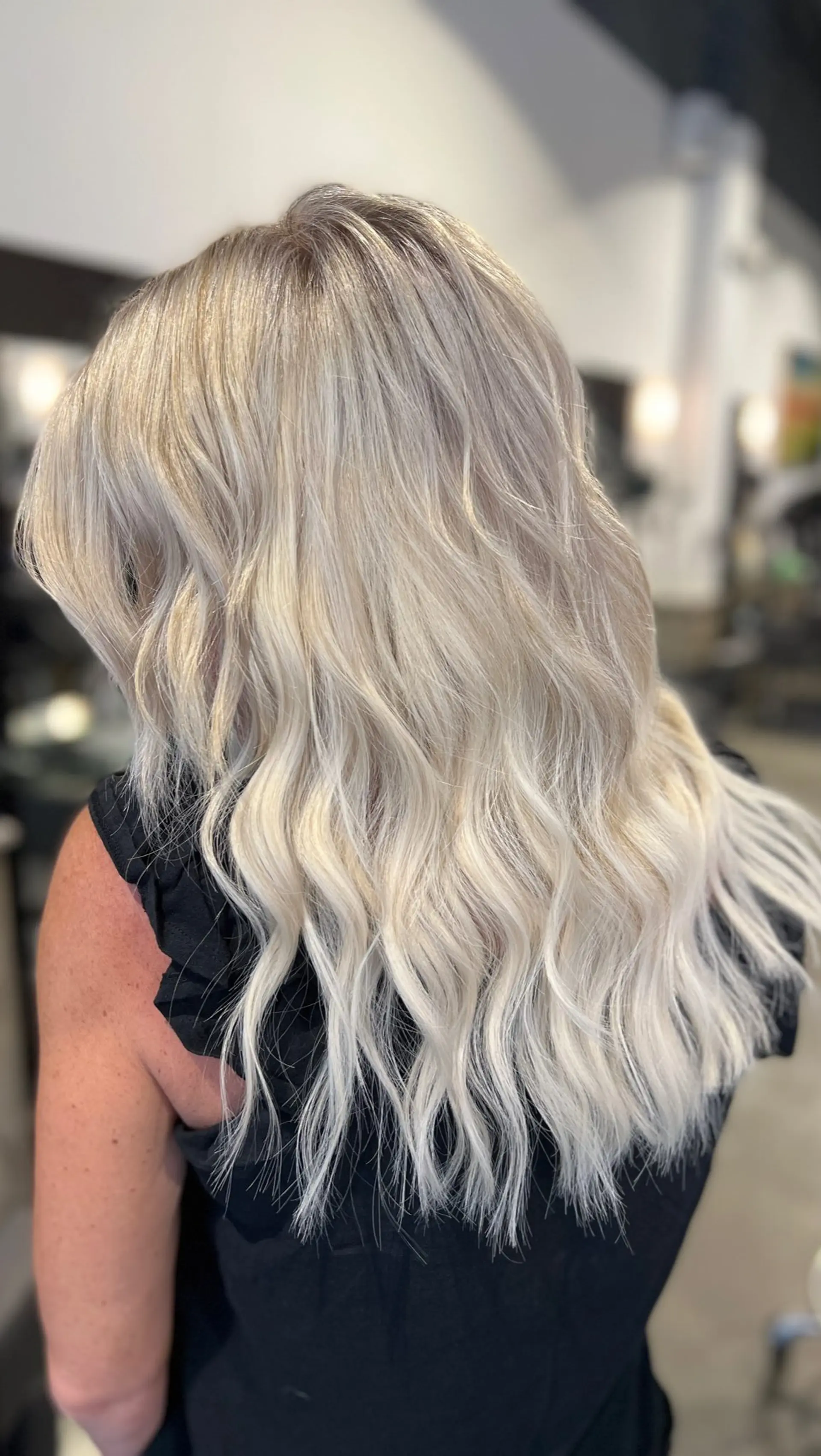 Long, bright icy platinum blonde hair styled into soft, textured beach waves with blended tape-in extensions. 1