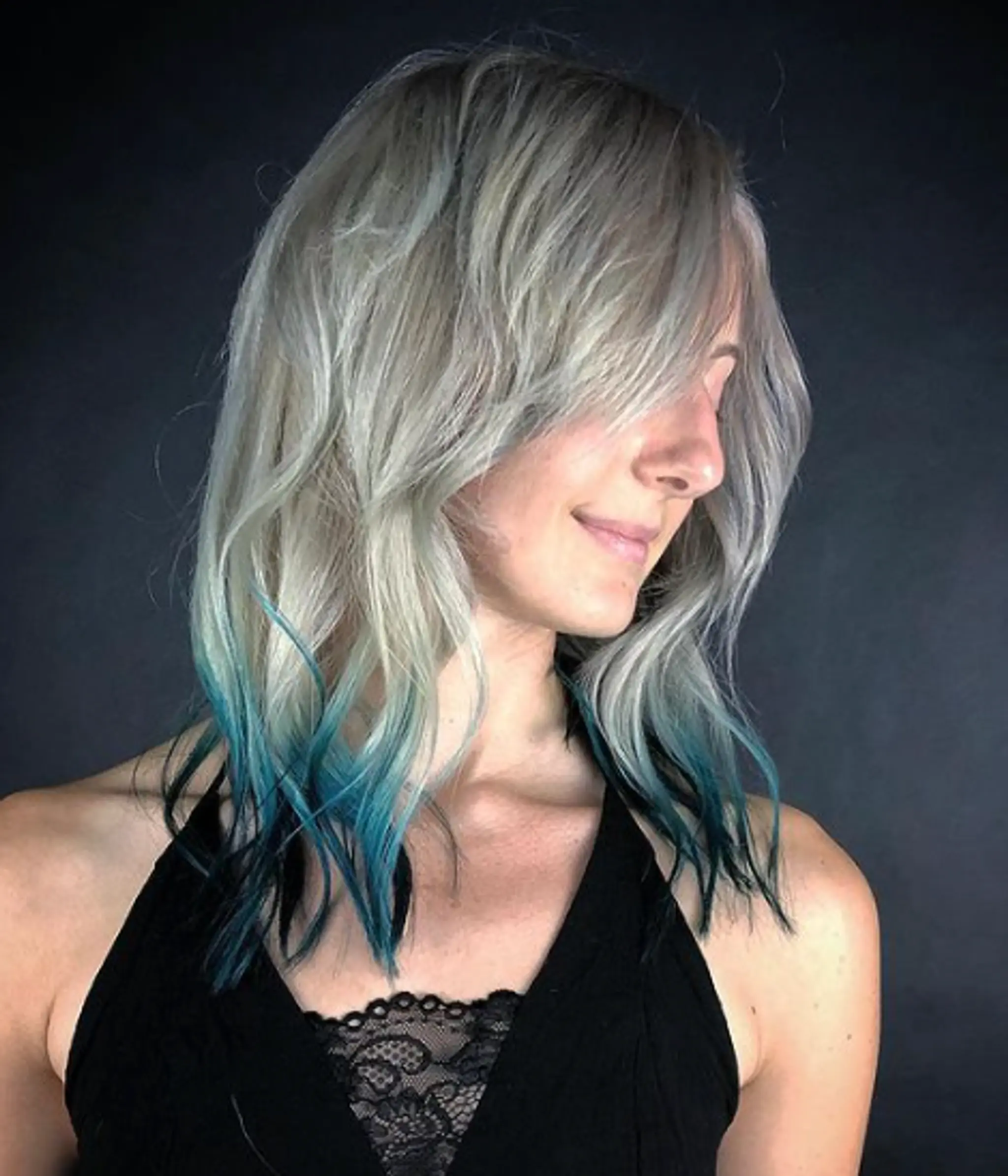 Medium-length wavy silver hair with teal tips, featuring an asymmetrical fringe and layered cuts.