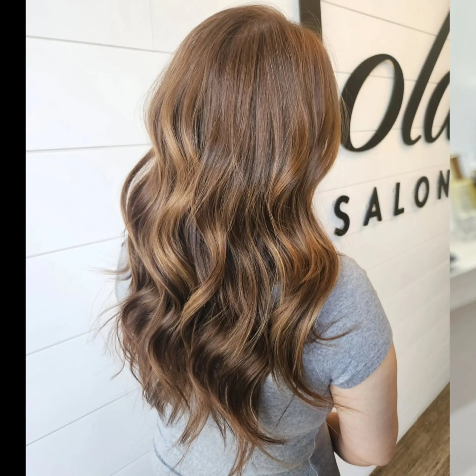 Long brown hair enhanced with seamless caramel balayage highlights and styled into loose, flowing waves. 1