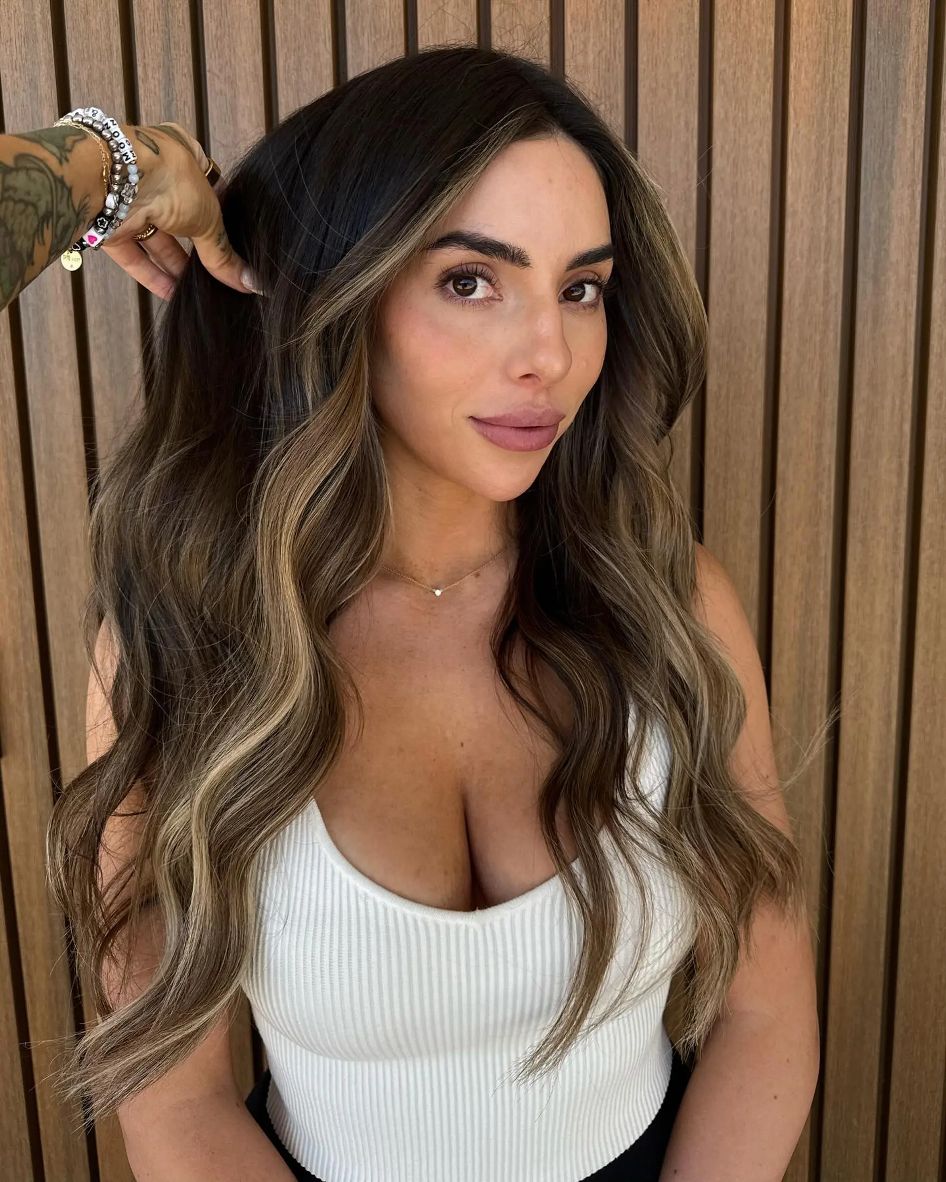 Long dimensional brunette hair styled in loose, voluminous waves with sun-kissed face-framing highlights. 1
