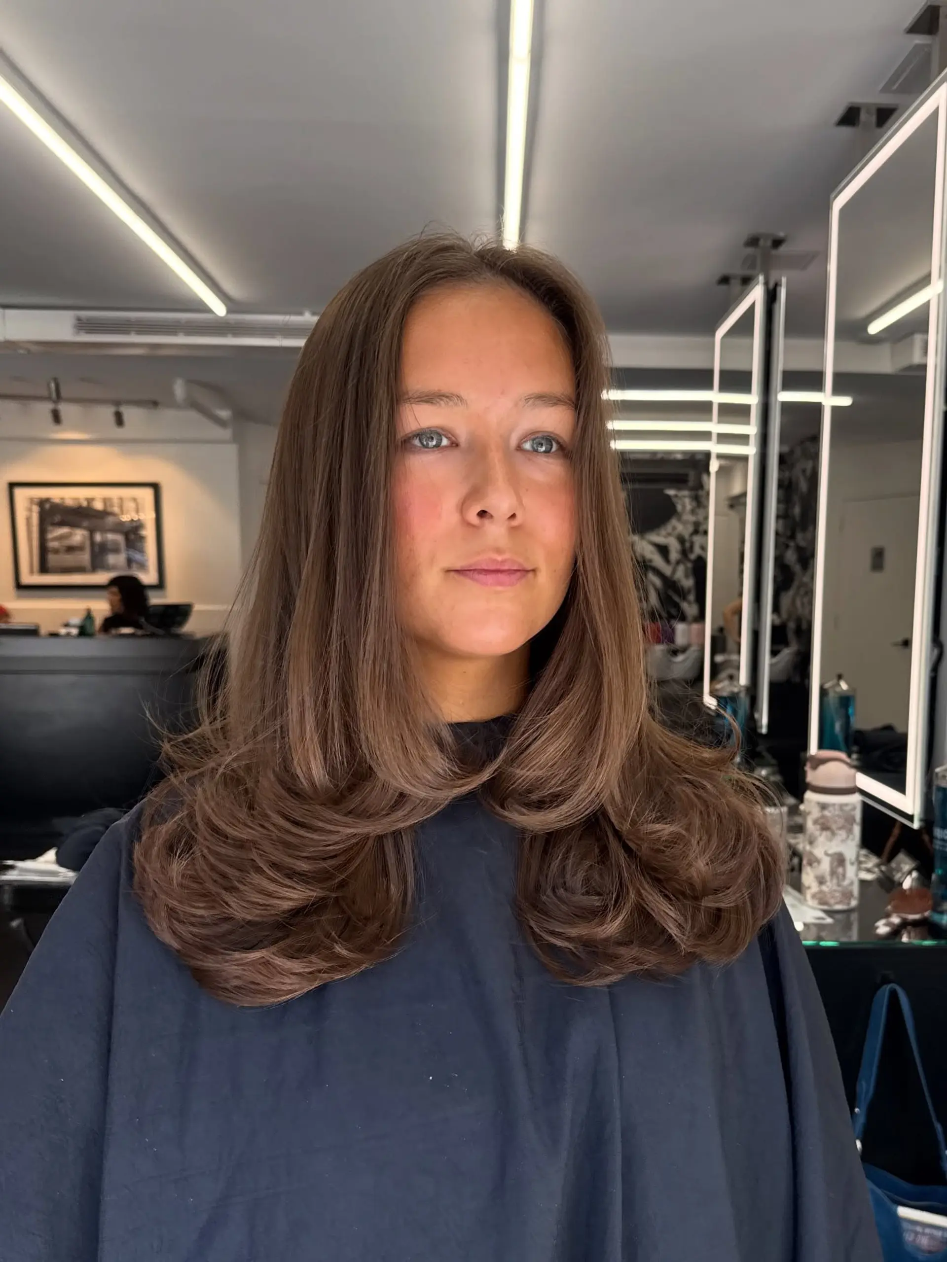 Long brunette hair styled in a bouncy, voluminous blowout with rounded, inward-curling ends and face-framing layers. 1