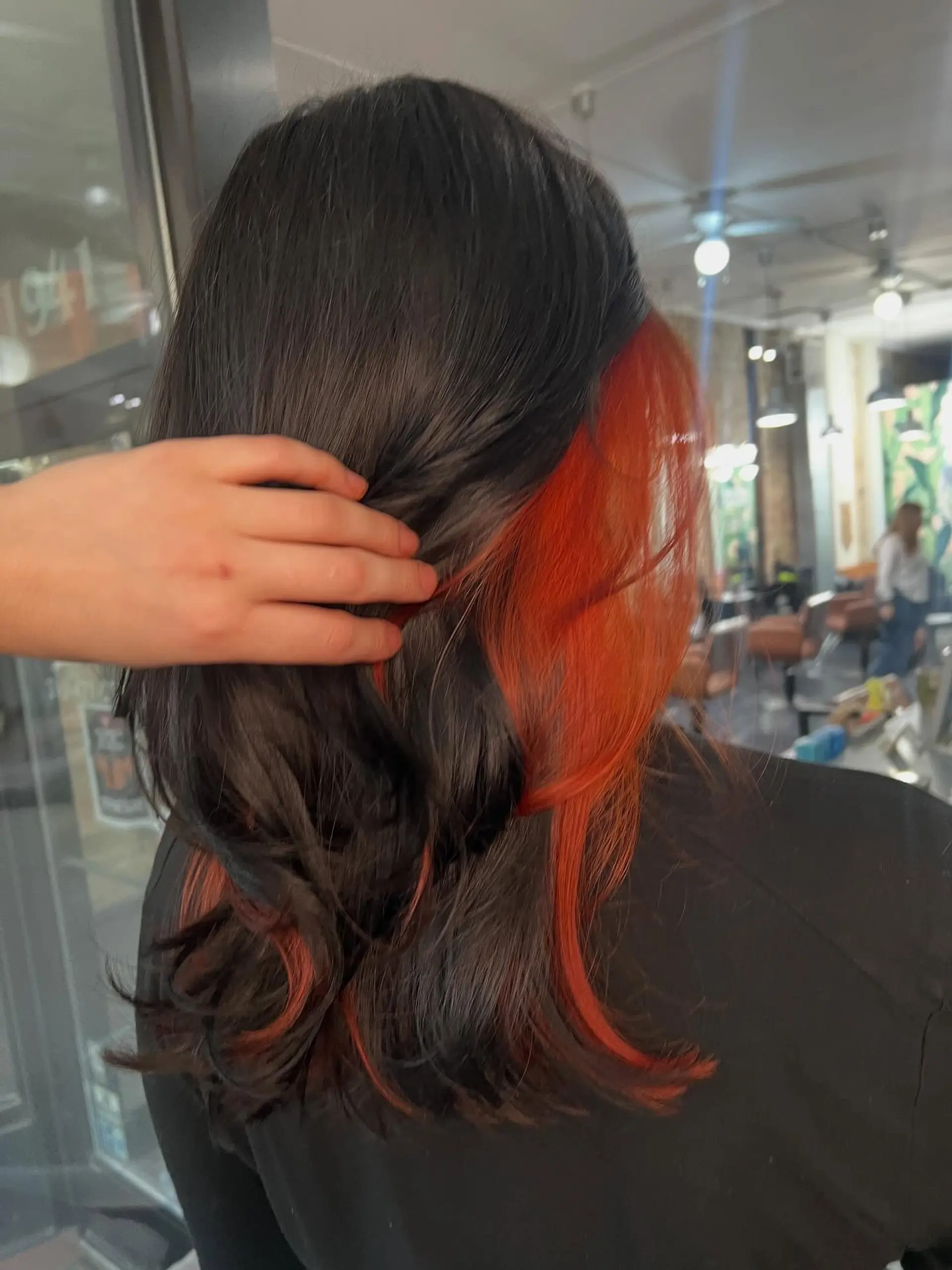 Medium-length dark black hair featuring a striking vibrant orange peekaboo underlayer revealed as the hair is lifted. 1